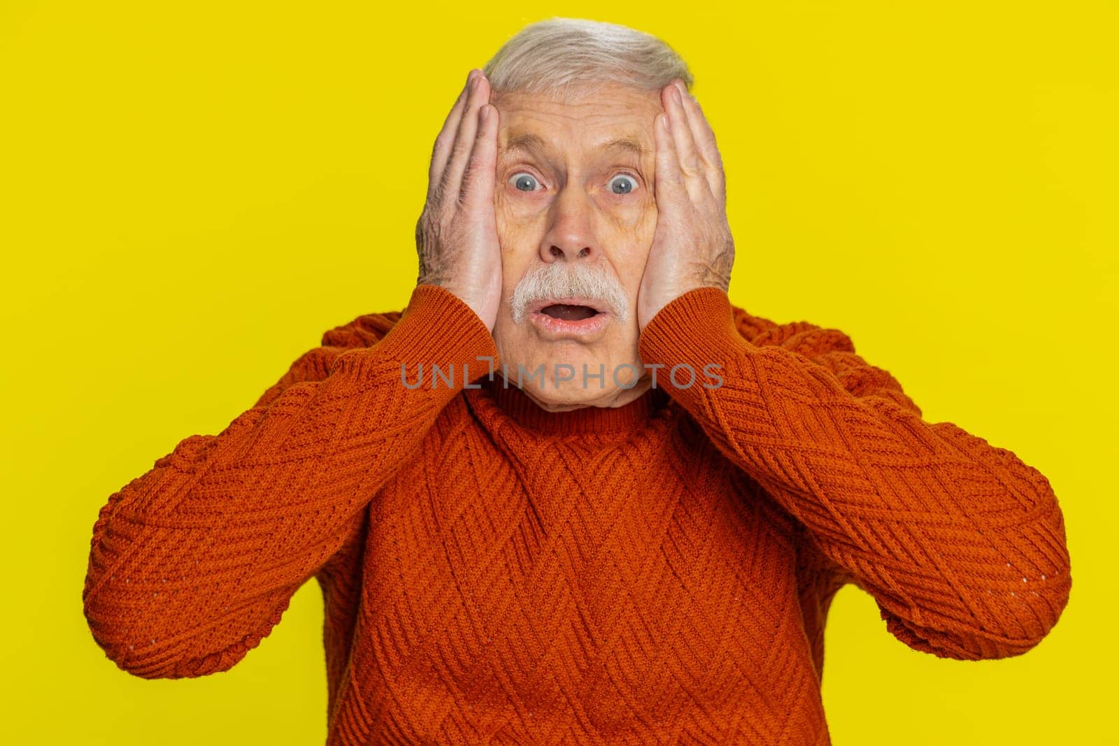 Oh my God, Wow. Excited amazed shocked senior man raising hands in surprise looking at camera with big eyes, shocked by sudden victory celebrating success achievement good news. Grandfather on yellow