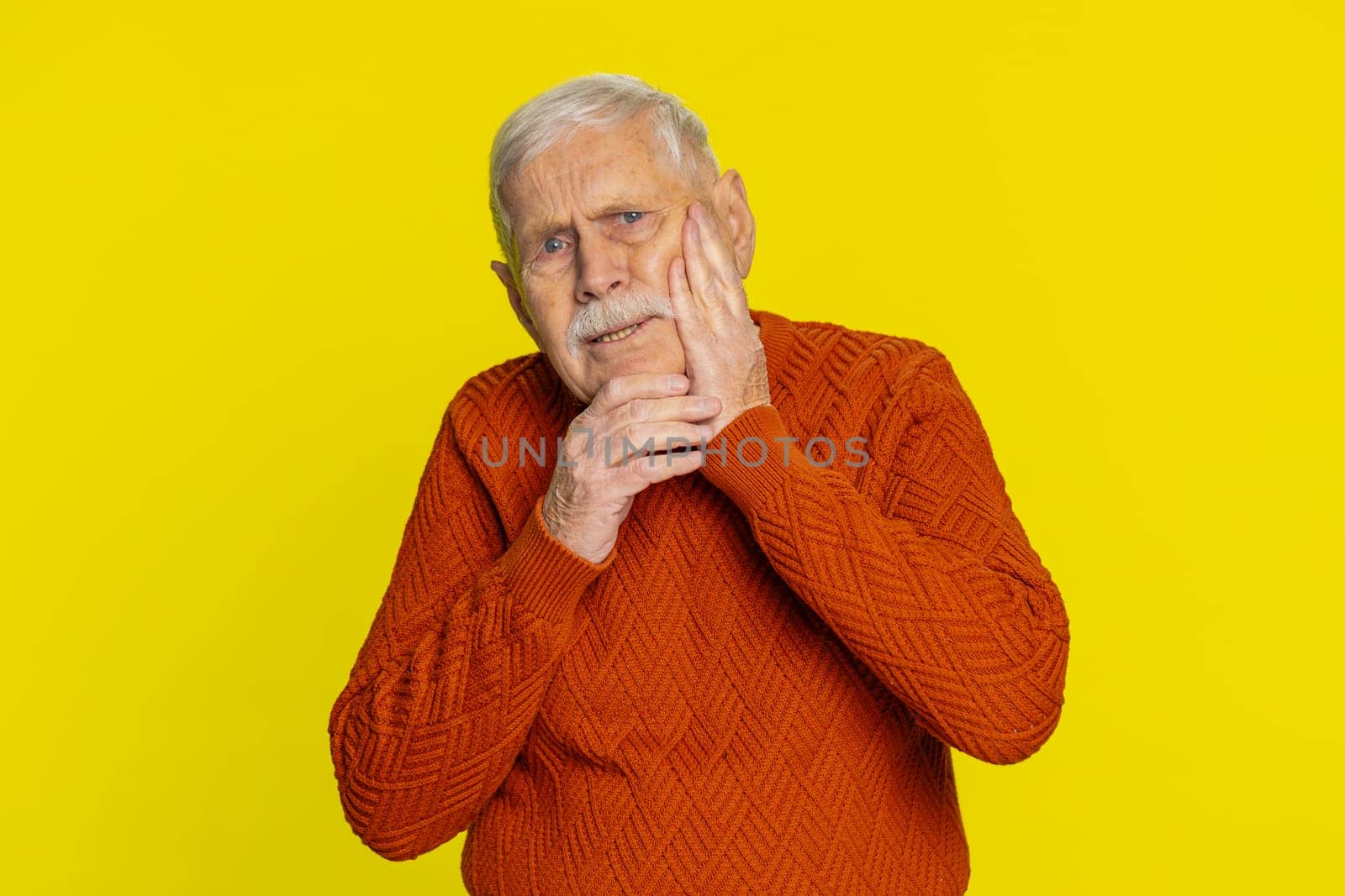 Dental problems. Senior old man touching cheek, closing eyes with expression of terrible suffer from painful toothache, sensitive teeth, cavities. Elderly grandfather pensioner on yellow background