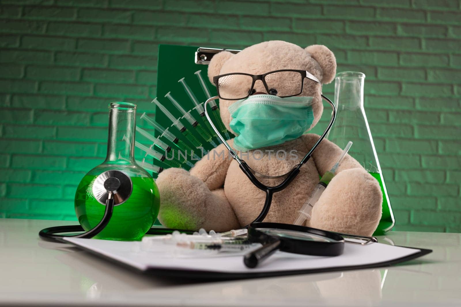 teddy bear in a medical mask with syringes in his shoulder on a white medical table with medical instruments