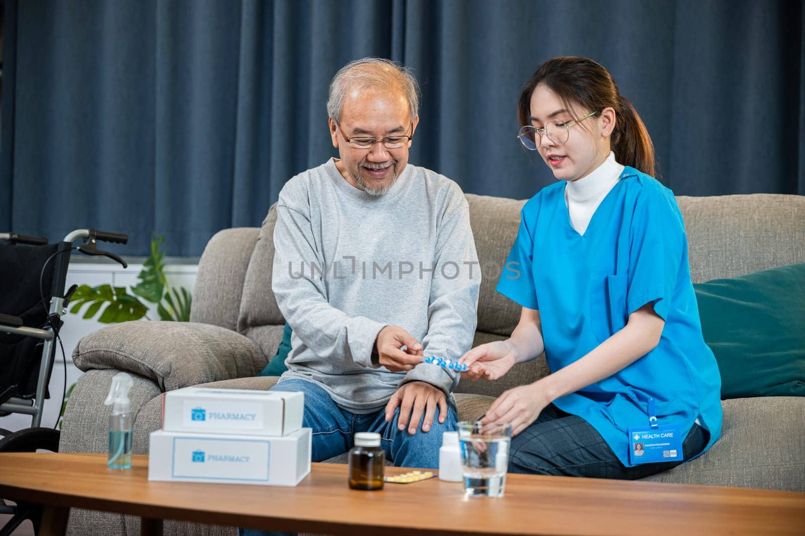 Asian nurse with physician explaining prescription medicine to attentive senior man at home by Sorapop