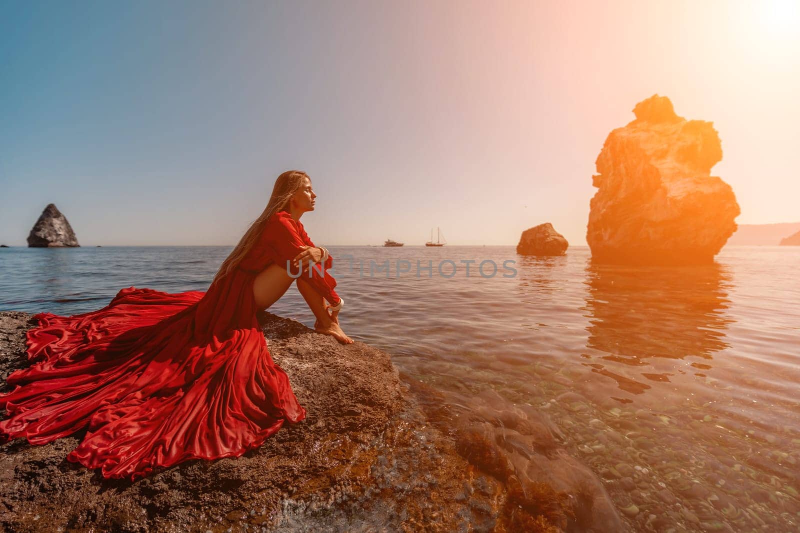 woman sea red dress. Beautiful sensual woman in a flying red dress and long hair, sitting on a rock above the beautiful sea in a large bay. by Matiunina