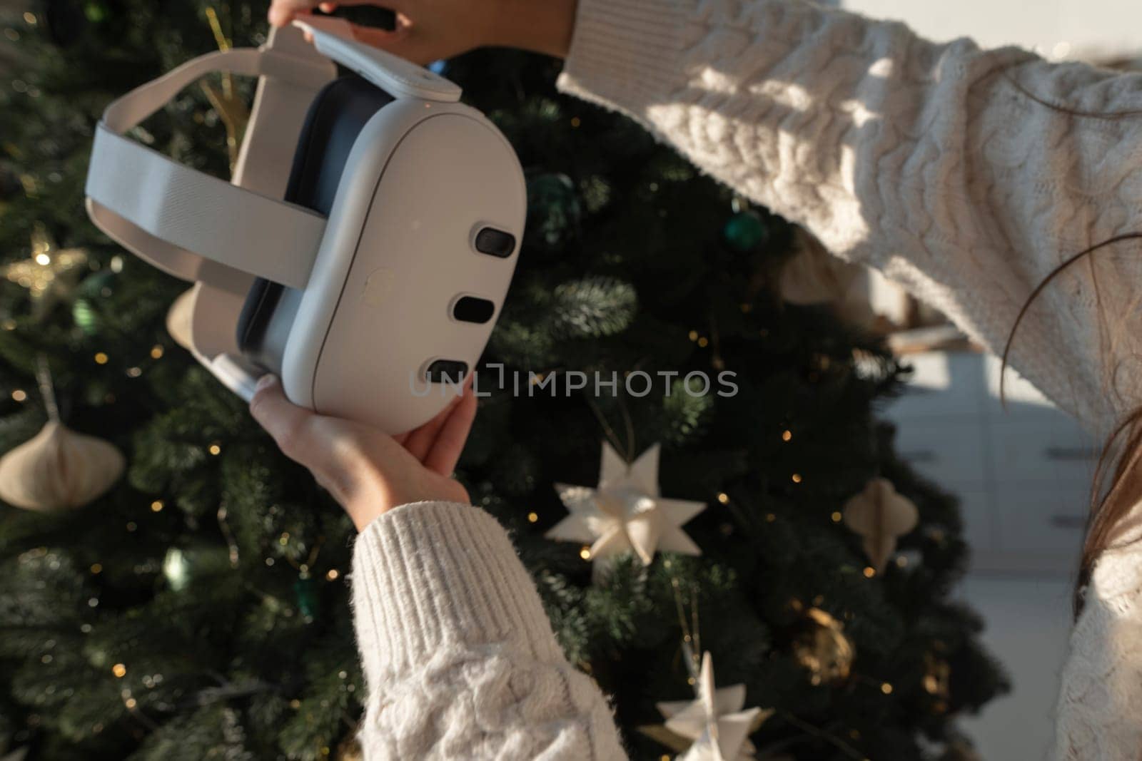 In front of a Christmas tree, a girl is holding a virtual reality headset. High quality photo