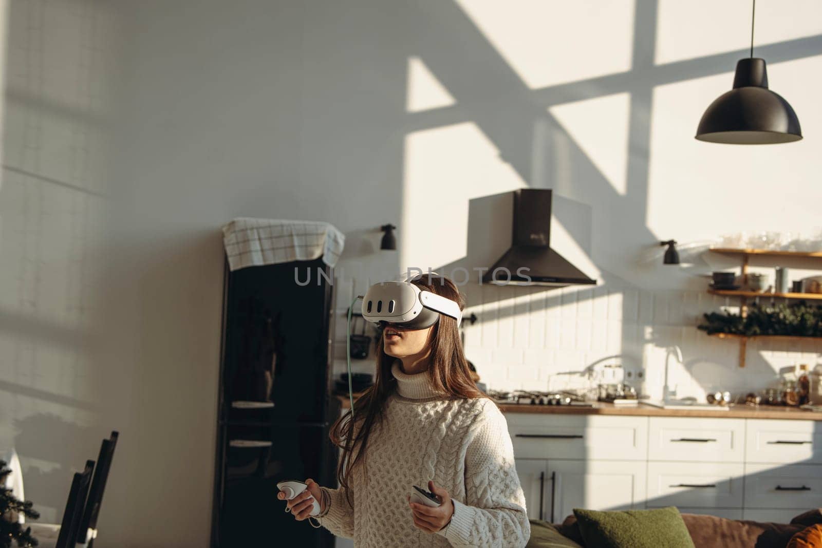 A stunning young woman plays an online game using a virtual reality headset in her apartment. by teksomolika