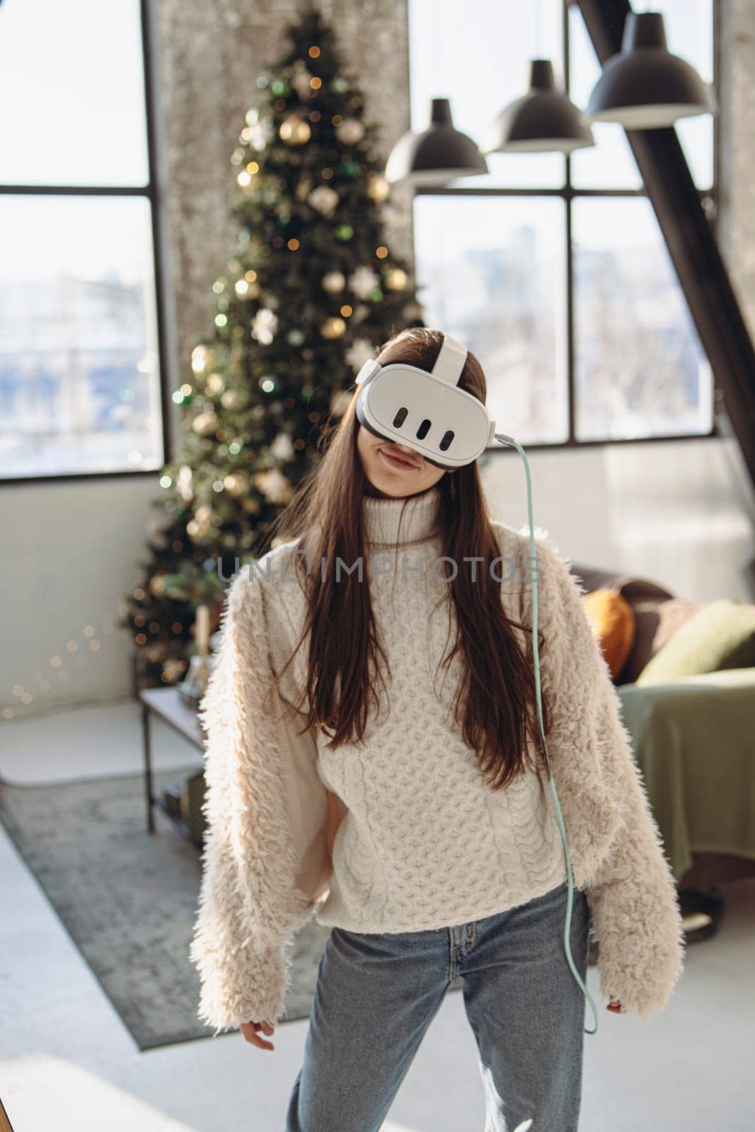 Immersed in virtual reality, a beautiful young woman stands beside a Christmas tree. by teksomolika
