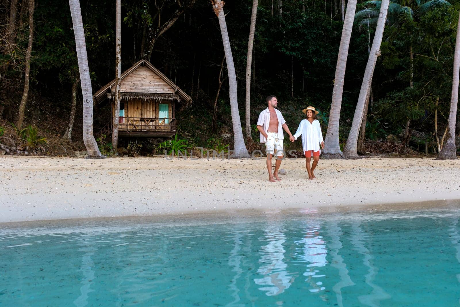 Koh Wai Island Trat Thailand near Koh Chang. couple walking in front of a wooden bamboo hut bungalow on the beach. a young couple of men and woman on a tropical Island in Thailand