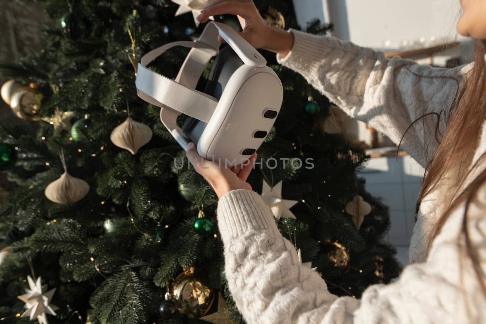 A Christmas tree forms the background as a girl holds a virtual reality headset. High quality photo