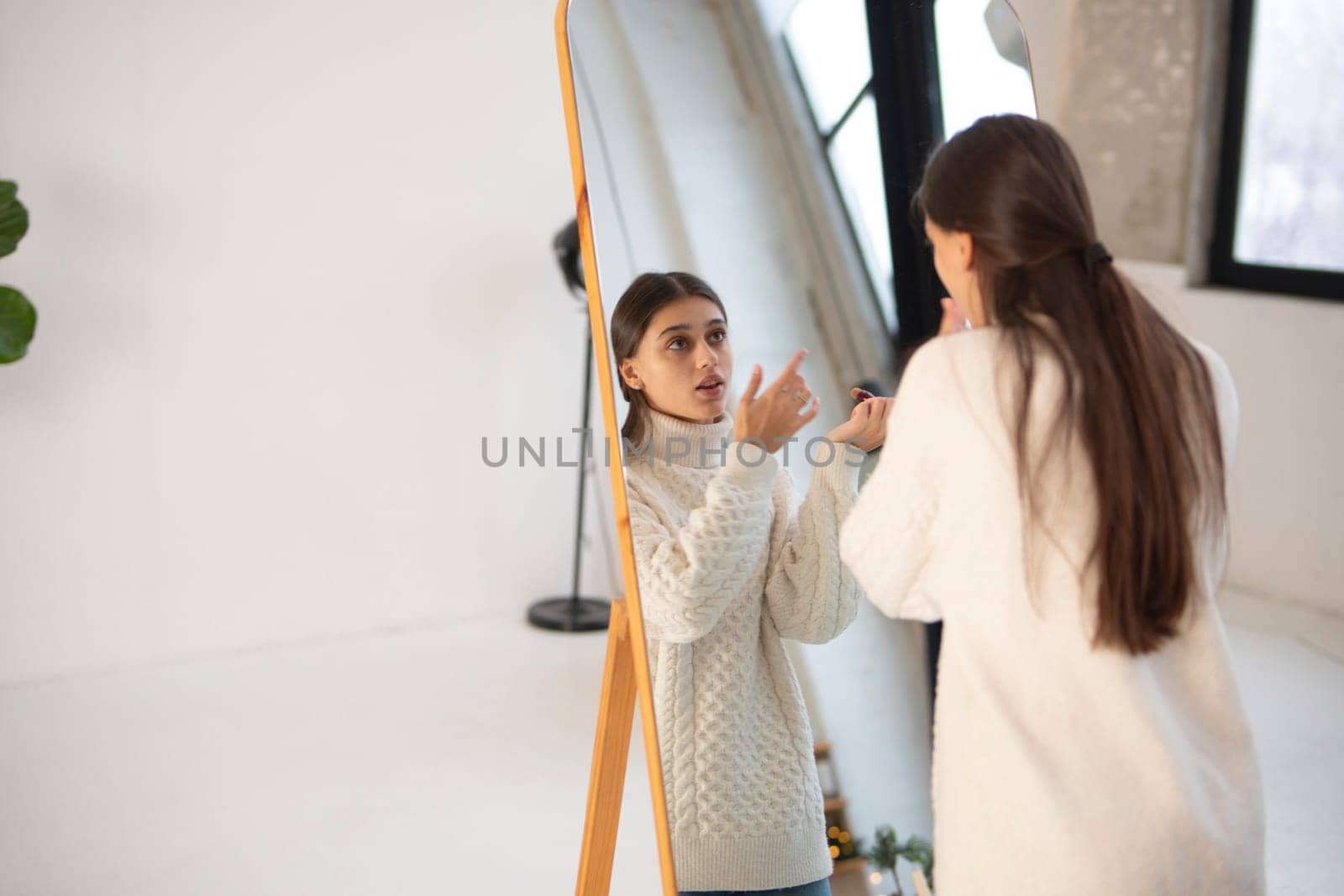 Embracing the Christmas spirit, a lovely young woman perfects her makeup at the mirror. by teksomolika