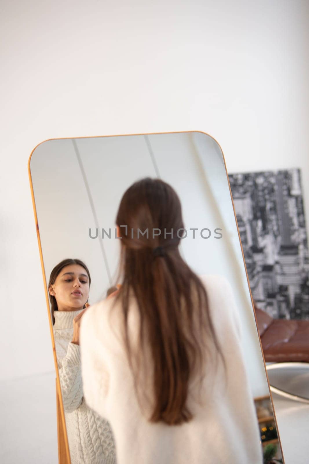 In a festive Christmas ambiance, a beautiful young woman does her makeup by the mirror. by teksomolika