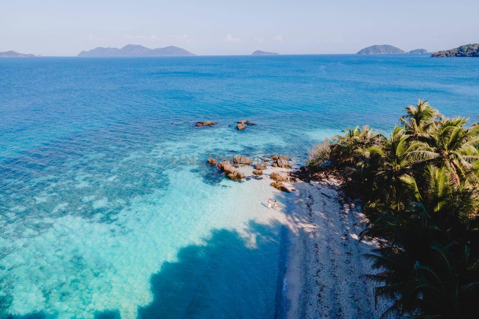 Drone aerial view at Koh Wai Island Trat Thailand. A young couple of men and women walking on a tropical beach during a luxury vacation in Thailand with a turqouse colored ocean