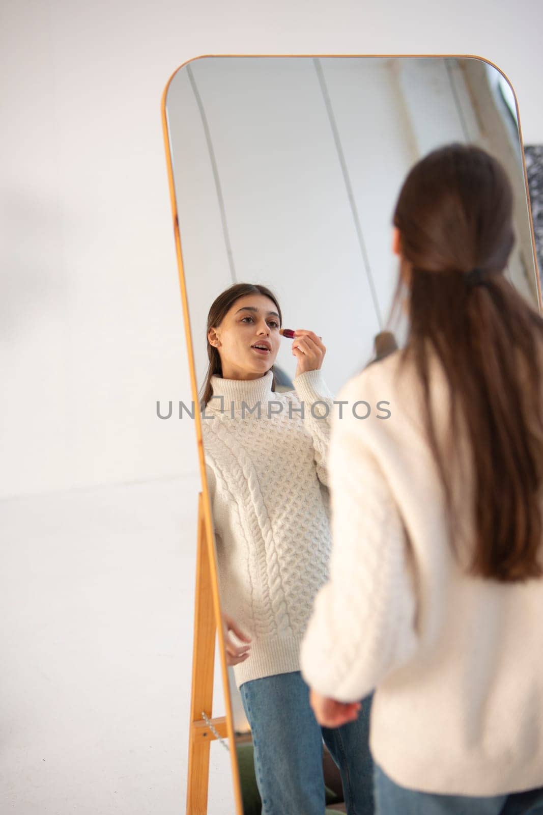 With Christmas cheer around, a stunning young girl works on her makeup in front of the mirror. High quality photo