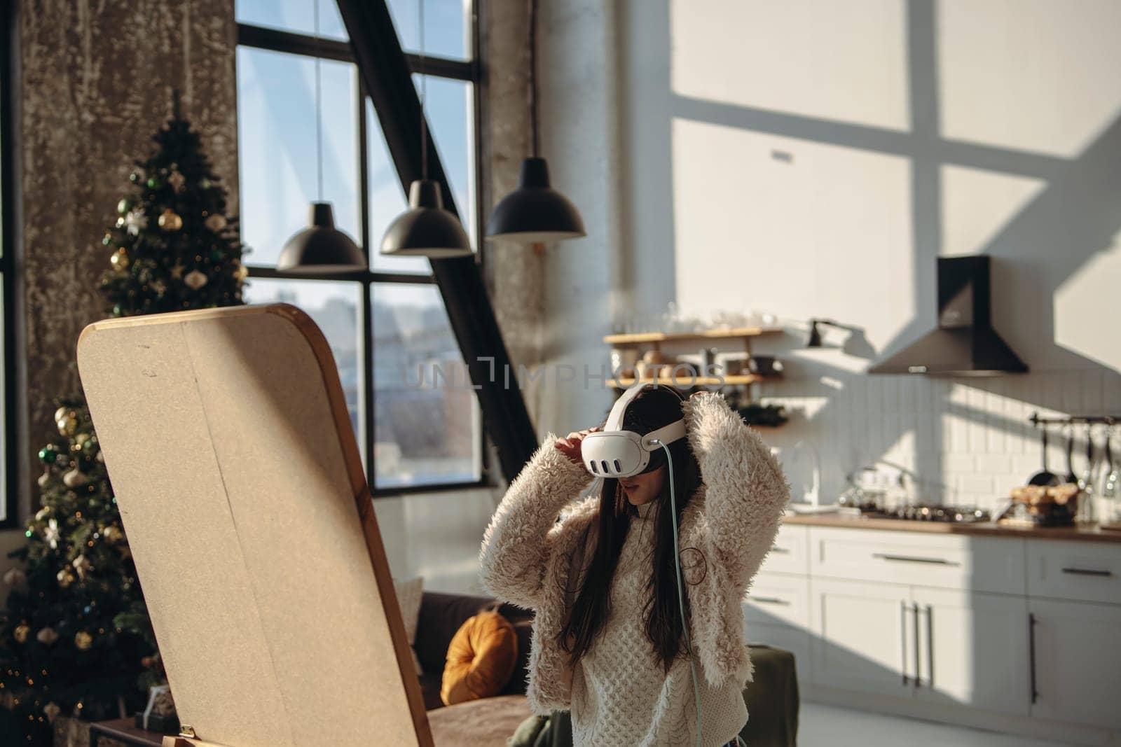 With sunlight flooding the room, a vibrant young lady stands with a virtual reality headset before the mirror. High quality photo