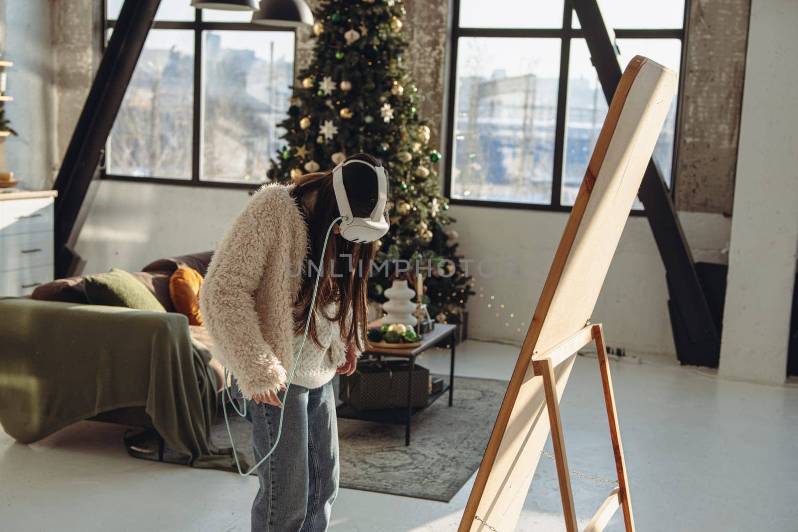 In a Christmas setting, a young woman in light clothing and a virtual reality headset stands in front of the mirror. High quality photo