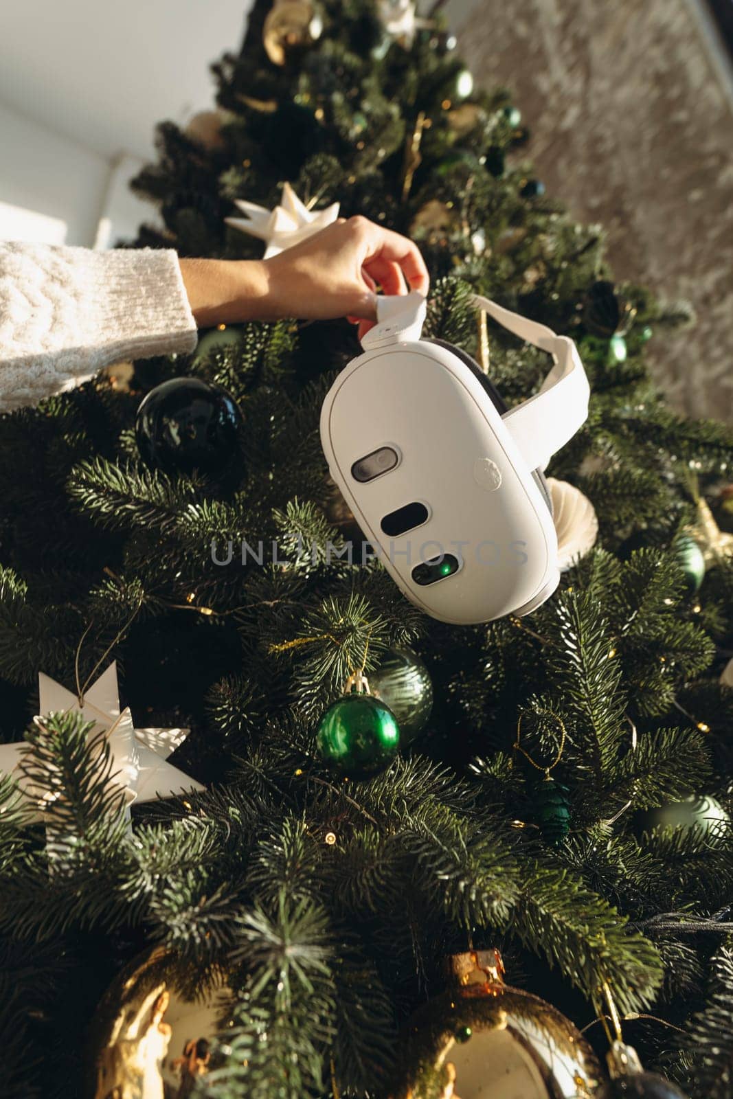 Amidst a Christmas tree, a girl is seen holding a virtual reality headset. by teksomolika