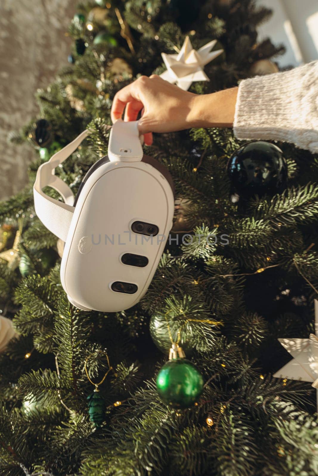 In the presence of a Christmas tree, a girl holds a virtual reality headset. High quality photo