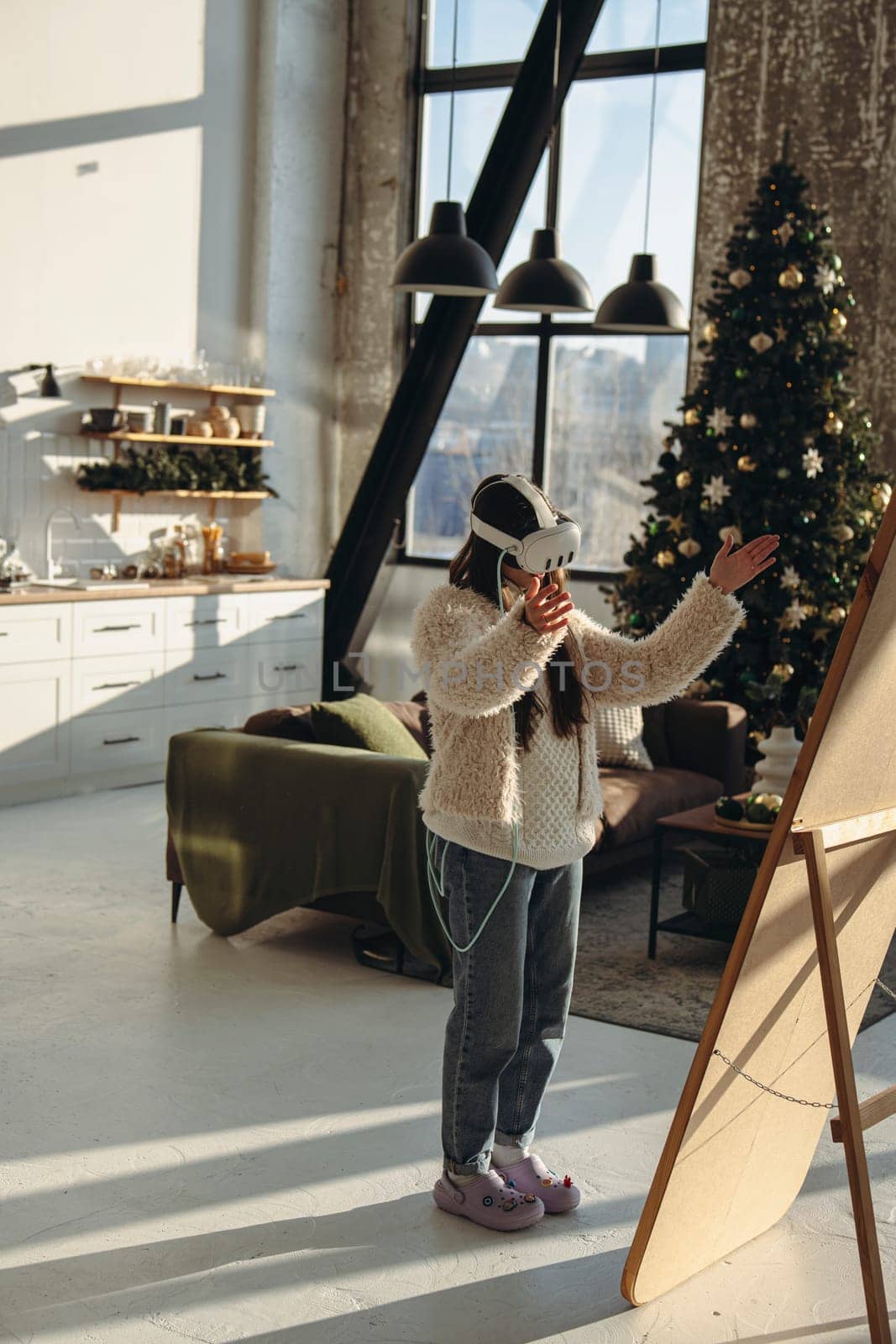 With the Christmas mood around, a young woman in light clothing and a virtual reality headset stands before the mirror. High quality photo