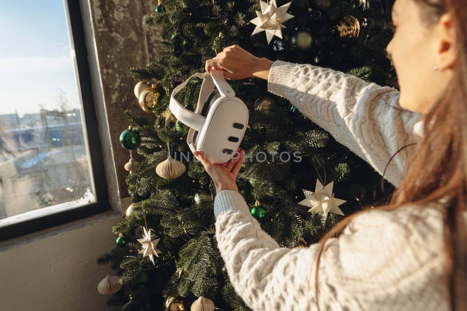 With a Christmas tree in the background, a girl is holding a virtual reality headset. High quality photo