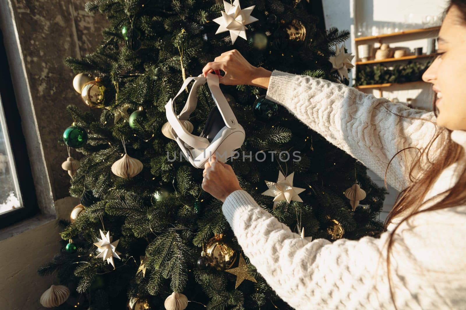 A girl, framed by a Christmas tree, holds a virtual reality headset. High quality photo