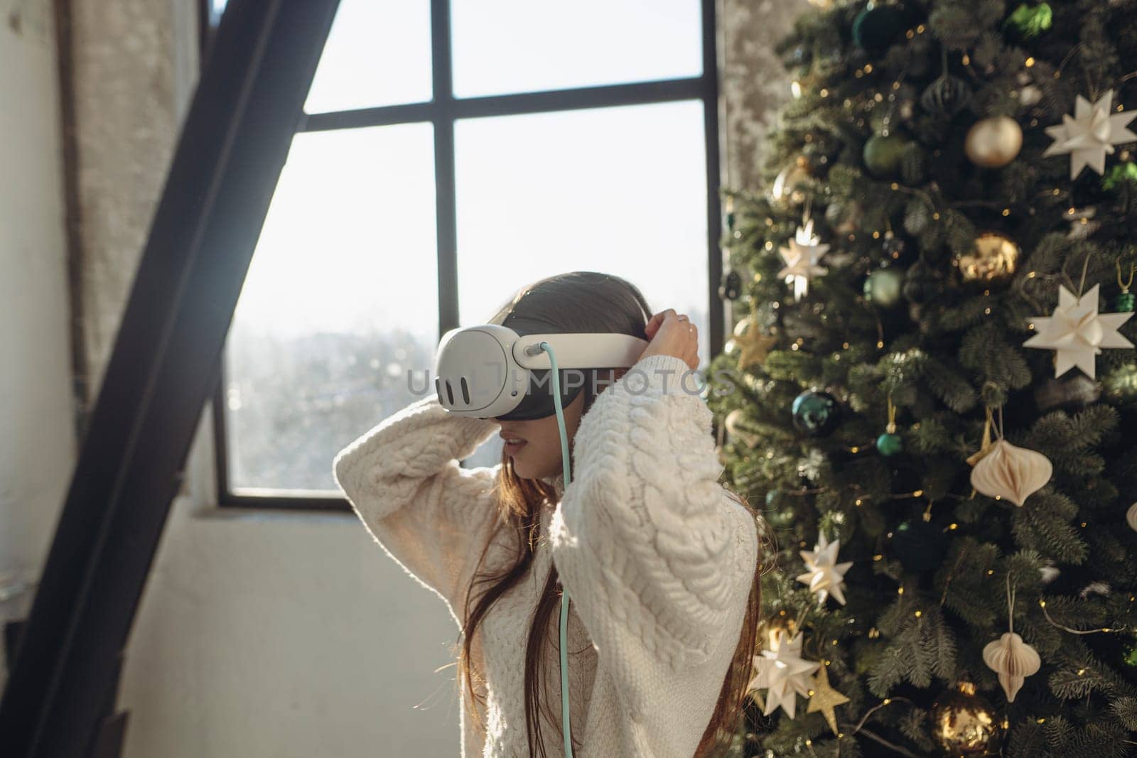 With sunlight streaming in, a vibrant young woman uses a virtual reality headset on a winter morning. by teksomolika