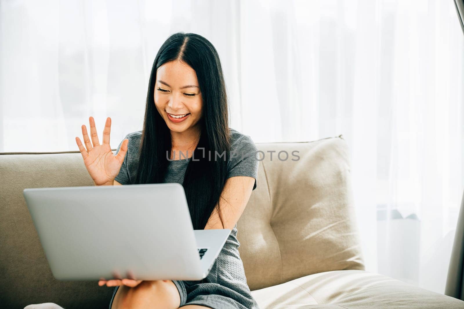Young woman at laptop waves in video call by Sorapop