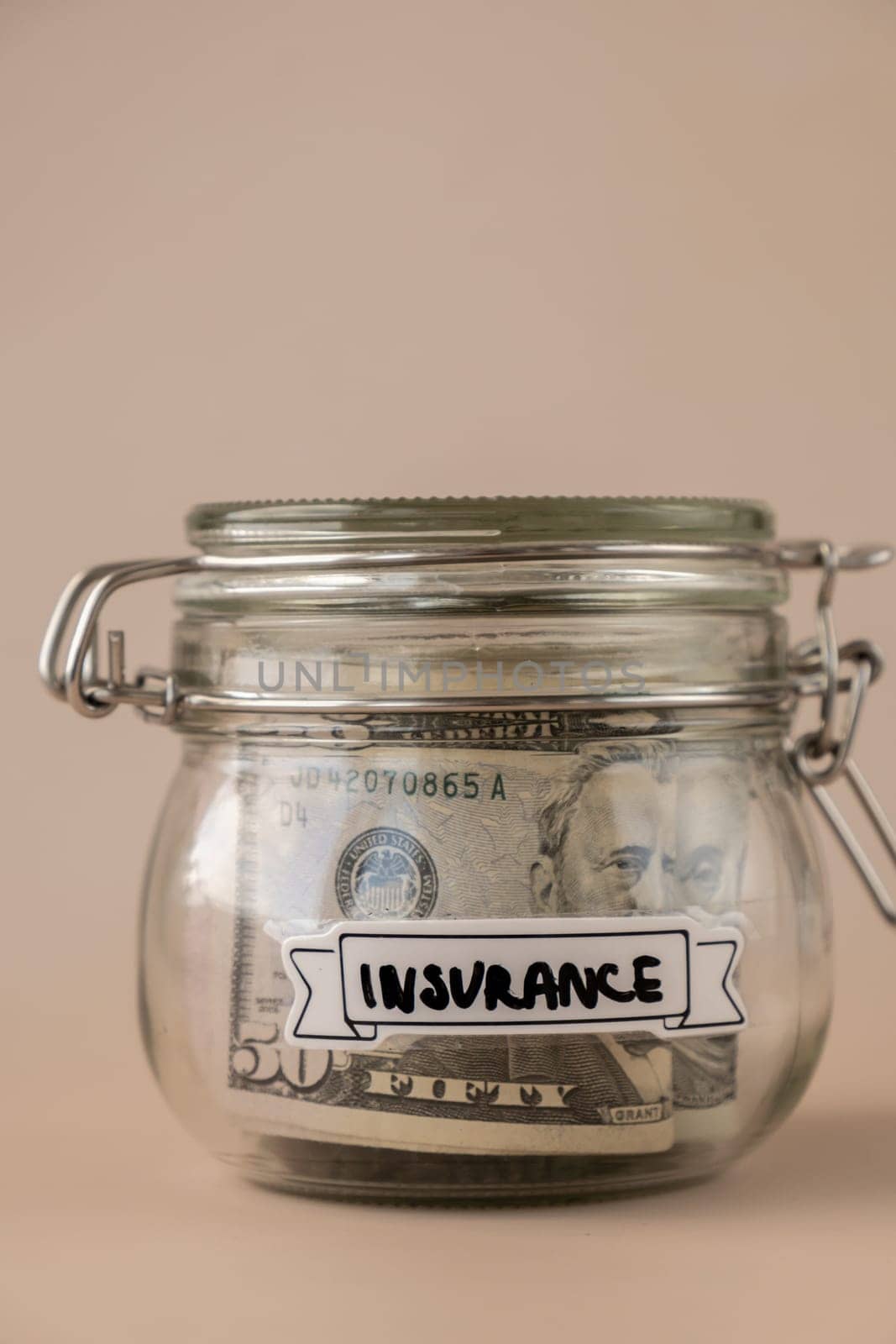 Saving Money In Glass Jar filled with Dollars banknotes. INSURANCE transcription in front of jar. Managing personal finances extra income for future insecurity. Beige background