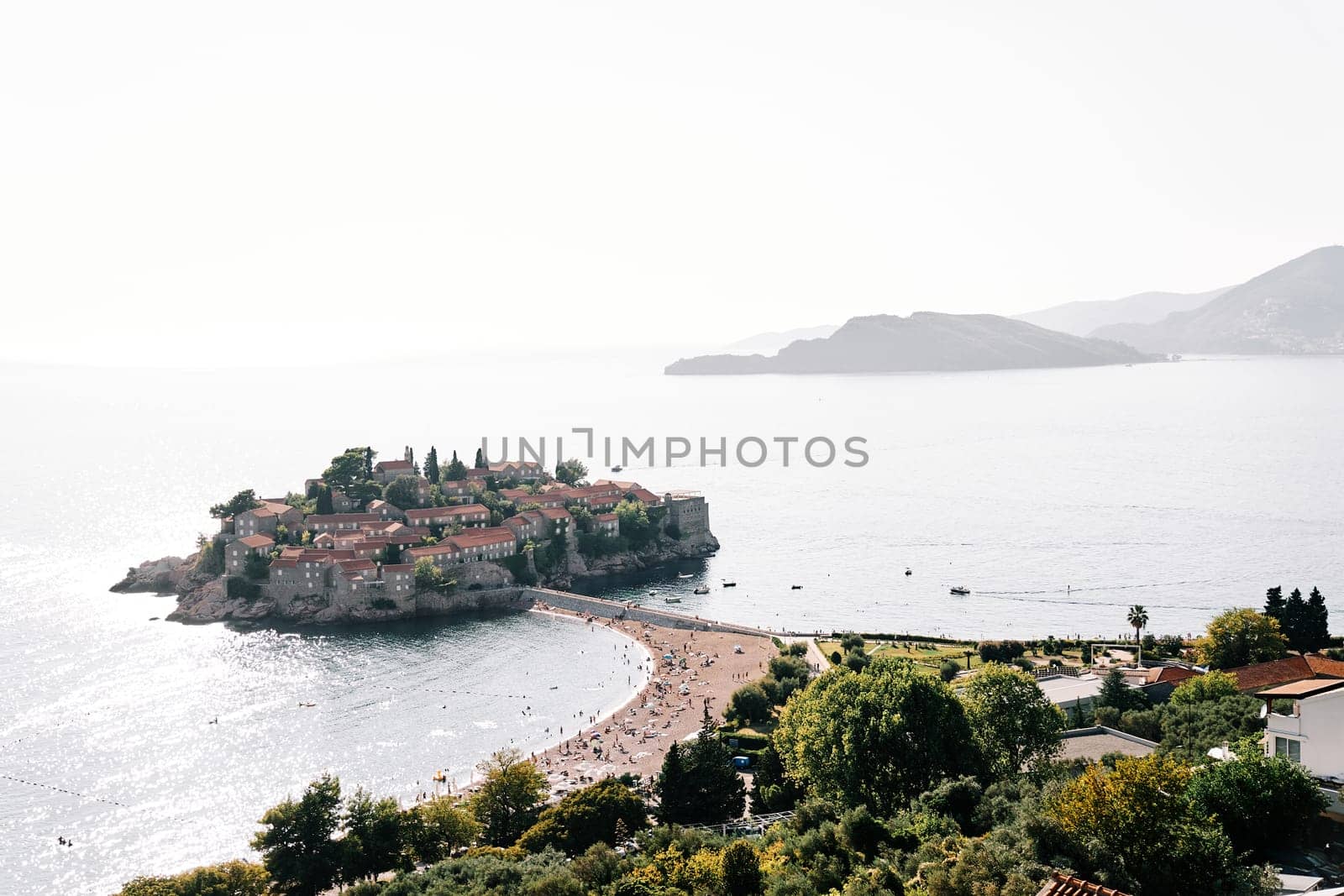 Tourists relax on the beach of the isthmus near the island of Sveti Stefan. Montenegro by Nadtochiy