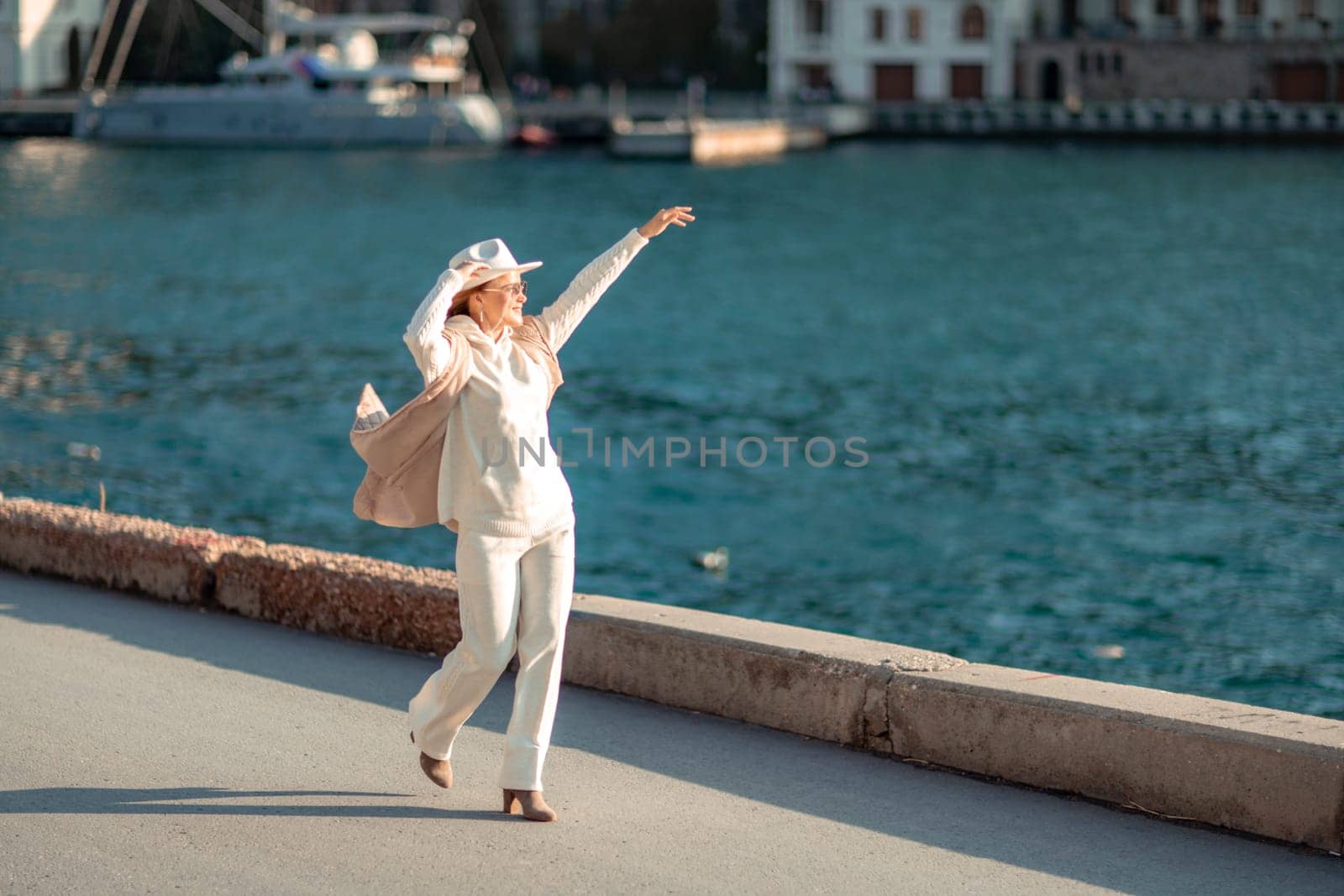 Happy blonde woman in a white suit and hat posing at the camera against the backdrop of the sea by Matiunina