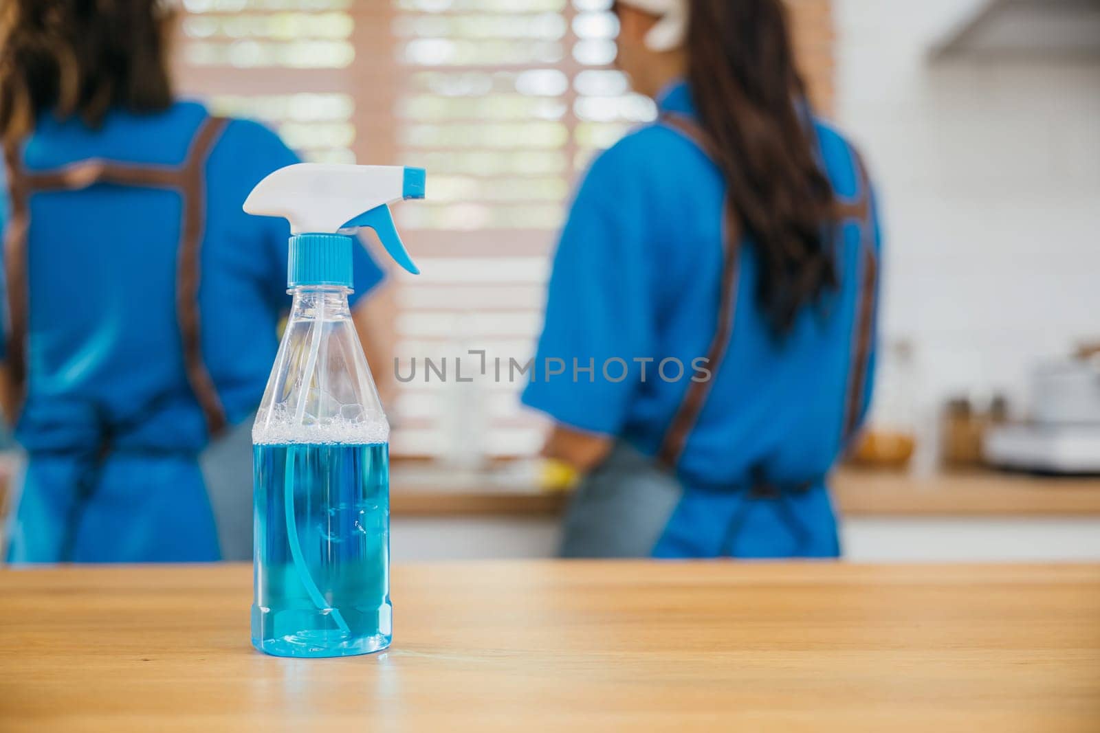 Occupied woman cleaning kitchen desk using spray product and towel. Housekeeping concept with a focus on hygiene and safety. Uniformed cleaner at work. Clean disinfect home care. Closeup spray bottle.