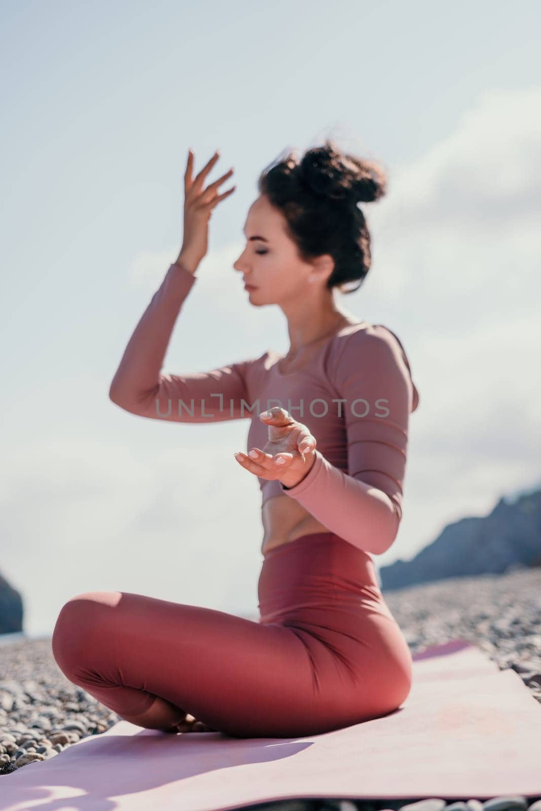 Middle aged well looking woman with black hair, fitness instructor in leggings and tops doing stretching and pilates on yoga mat near the sea. Female fitness yoga routine concept. Healthy lifestyle by panophotograph