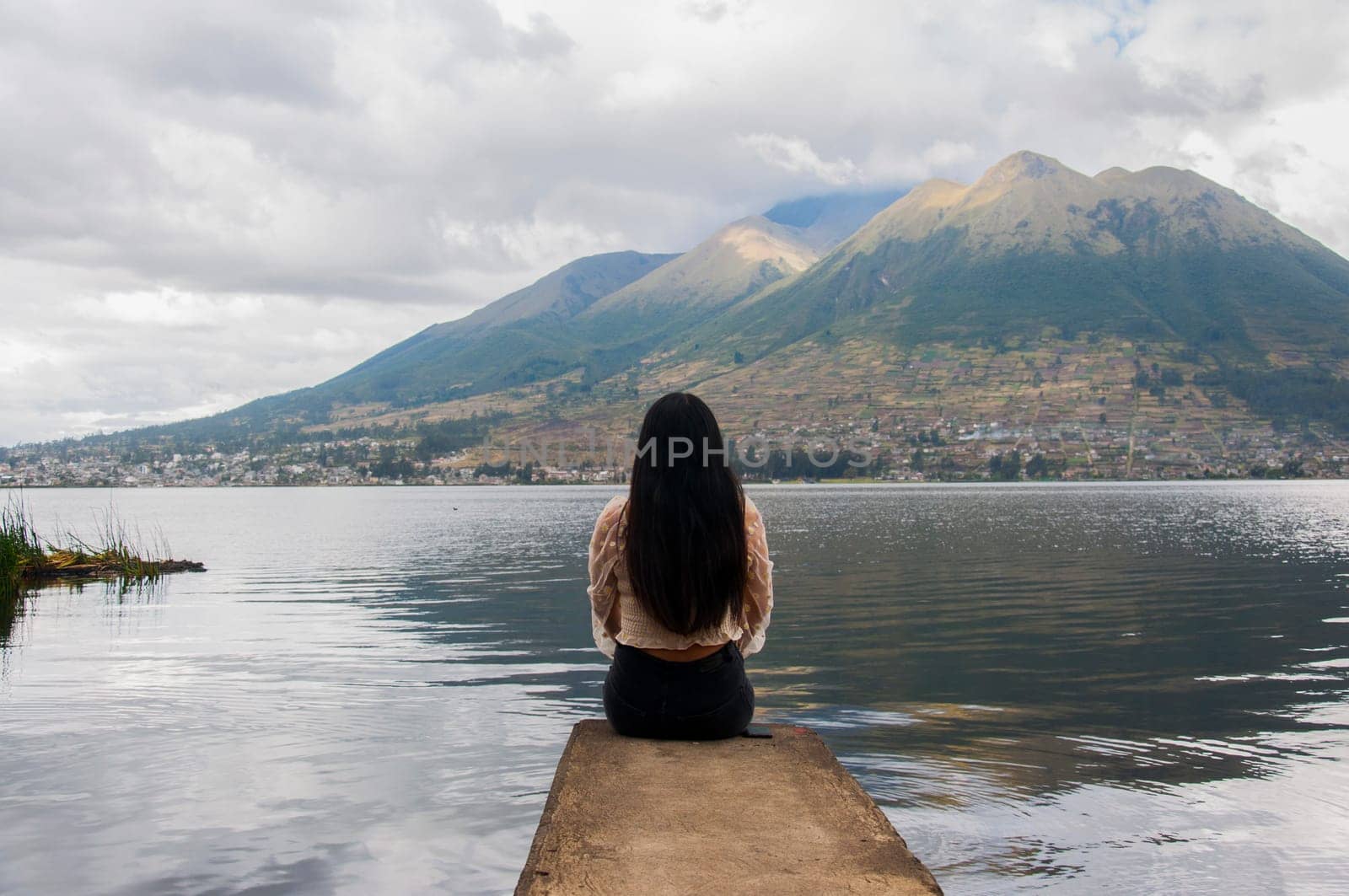 young latina with long hair with her back to the camera at the edge of a lake having a moment of calm, peace and relaxation looking at a dormant volcano in front of her. High quality photo
