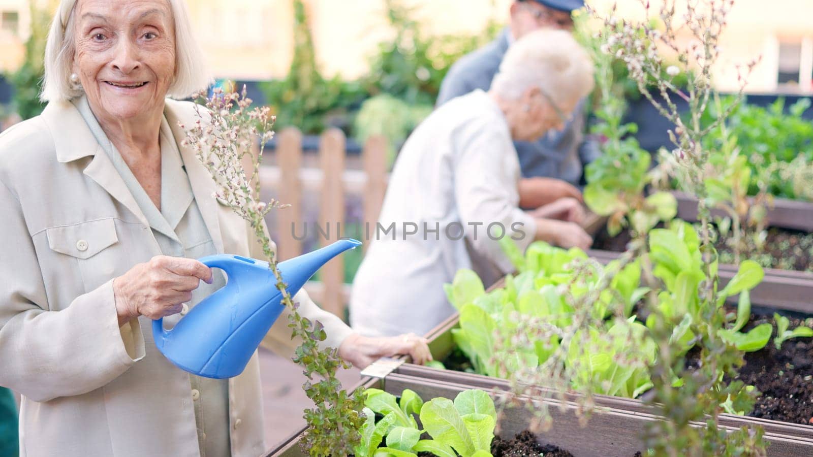 Picture of an old woman smiling while watering a garden in a geriatric