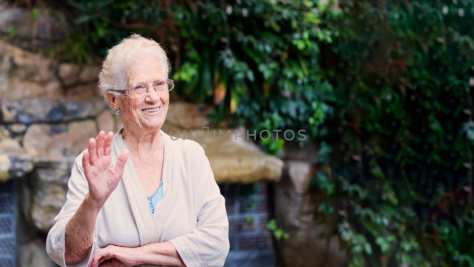 Photo with copy space of a grandmother waving and smiling in a garden