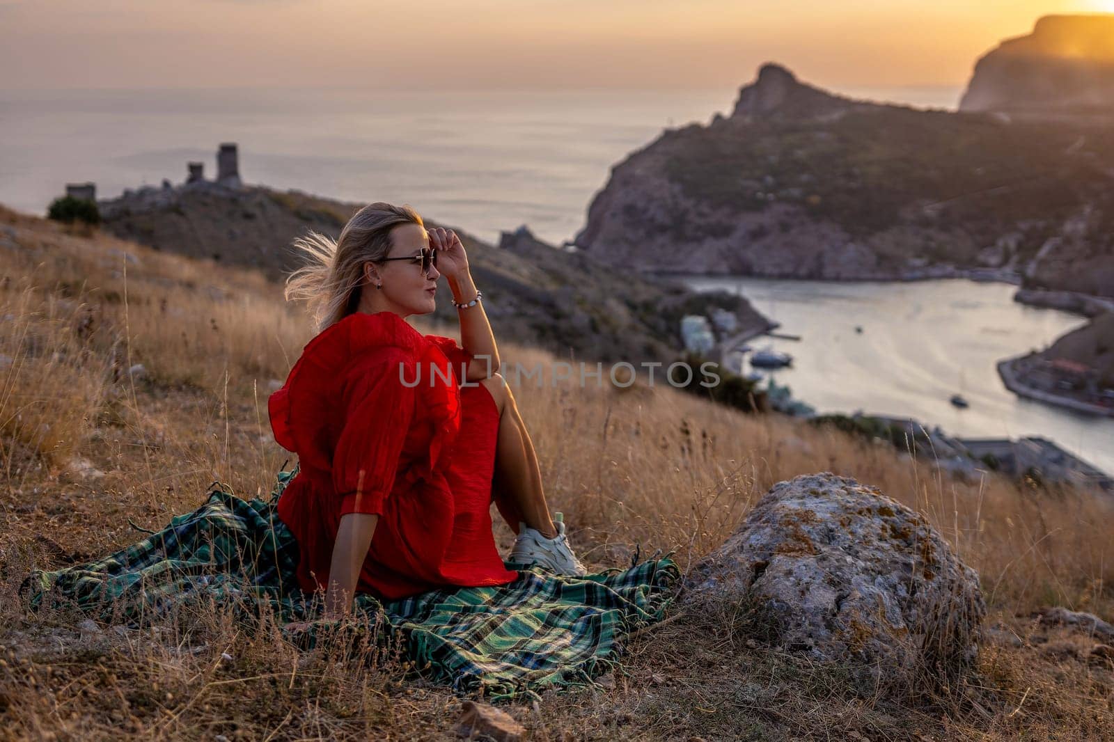 Woman sunset sea mountains. Happy woman siting with her back on the sunset in nature summer posing with mountains on sunset, silhouette. Woman in the mountains red dress, eco friendly, summer landscape active rest.