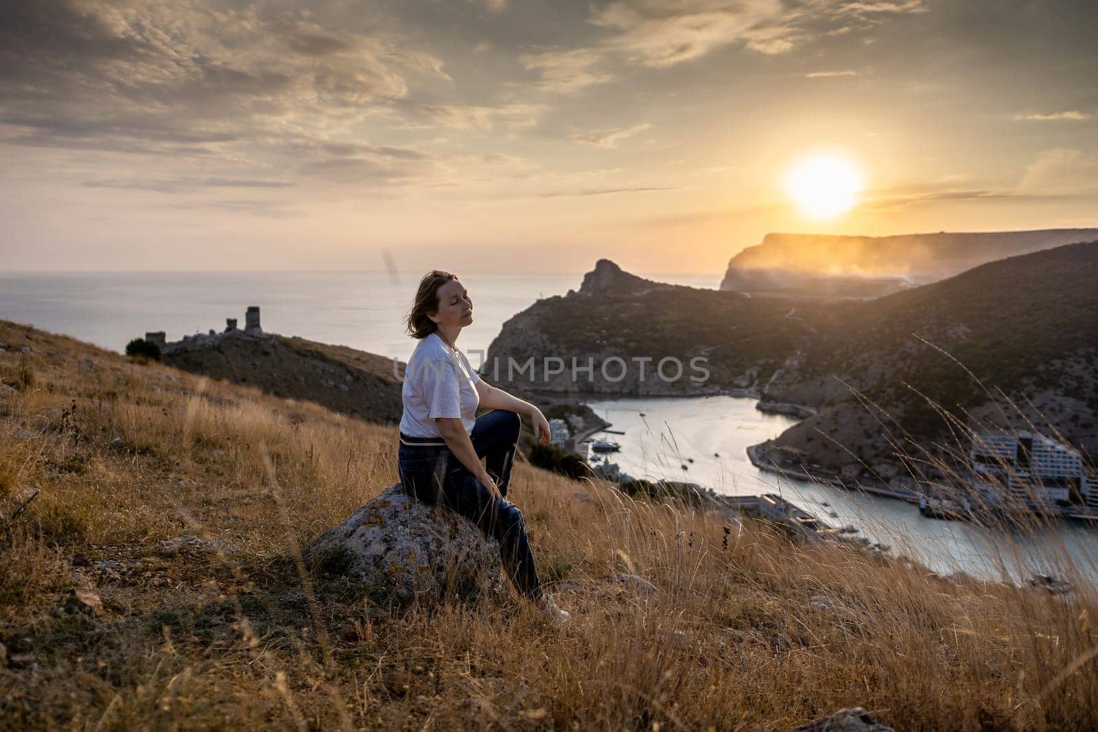 Happy woman on sunset in mountains. Woman siting with her back on the sunset in nature in summer. Silhouette. by Matiunina