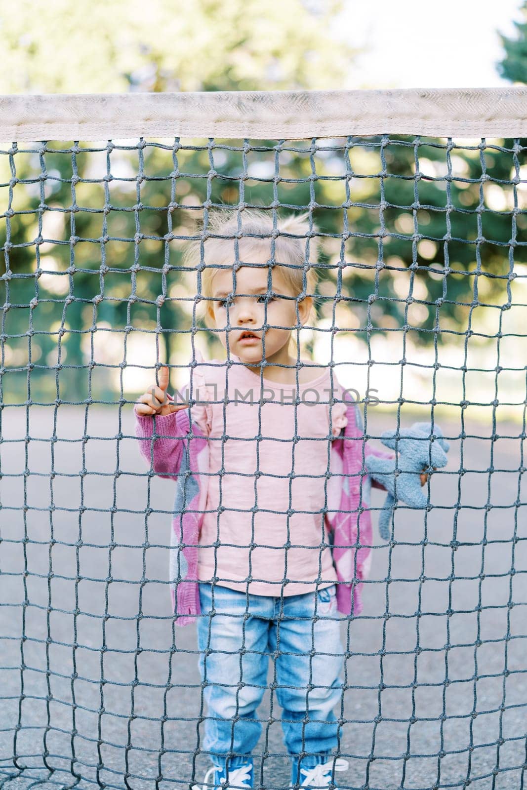 Little girl looks through the cells of the net holding onto it with her fingers by Nadtochiy