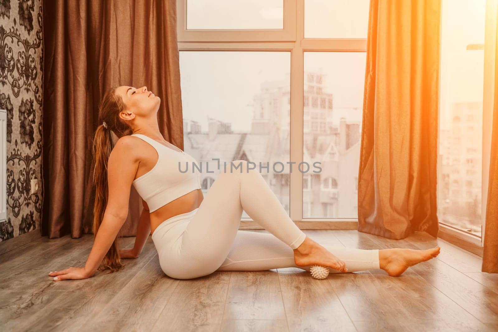 Middle aged athletic attractive woman practicing yoga. Works out at home or in a yoga studio, sportswear, white pants and a full-length top indoors. Healthy lifestyle concept.