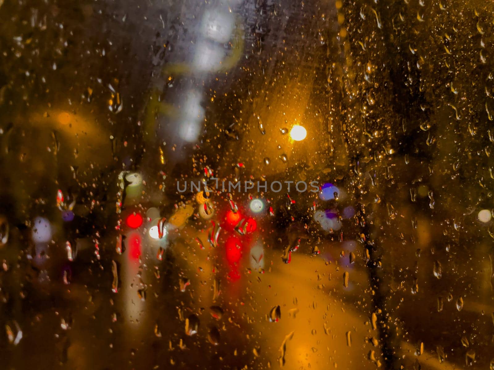 Rain bokeh road lights. Abstract shot of evening city traffic bokeh. Multicolored lights of the evening city and passing cars through a wet rainy window