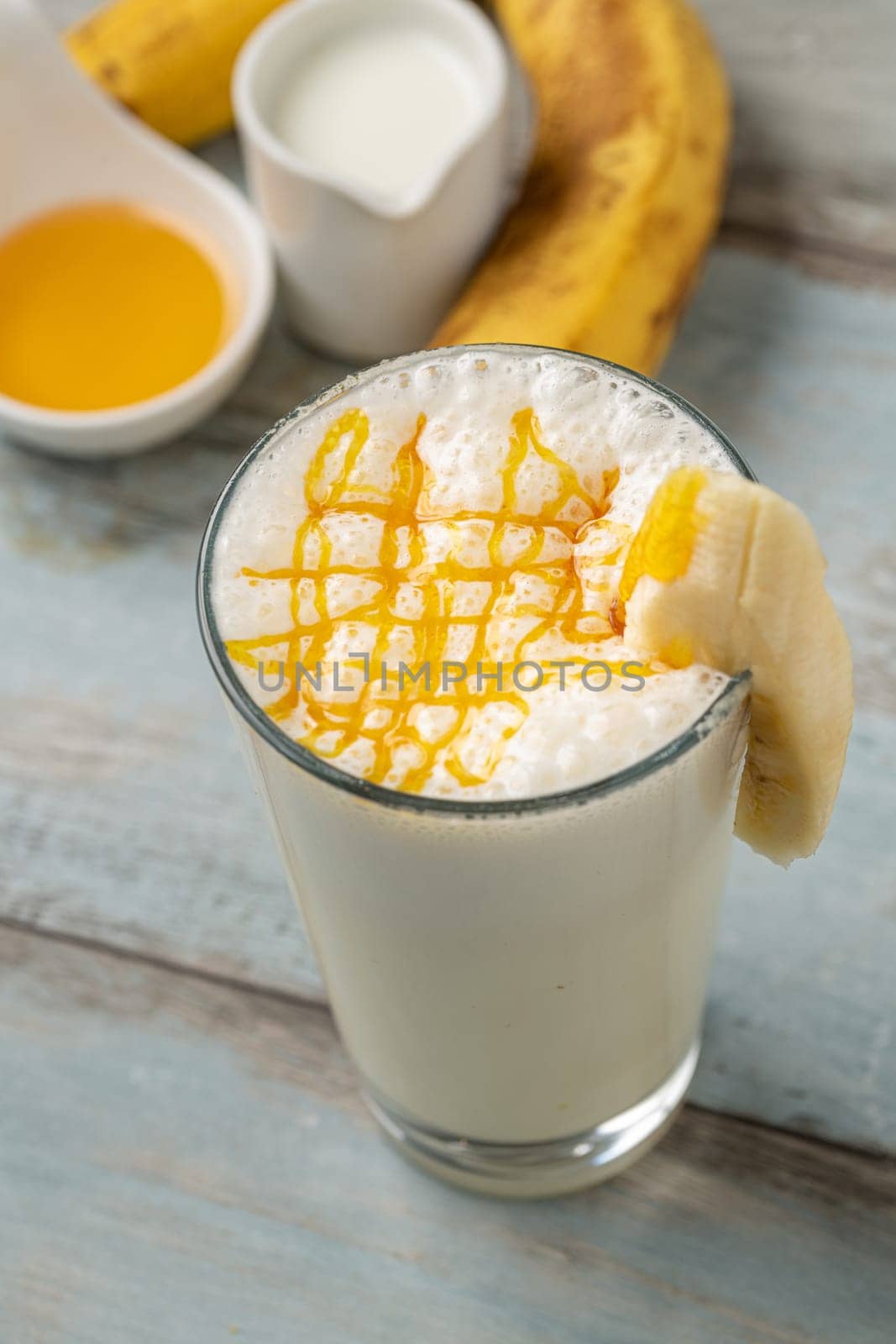 Milk with honey and banana in glass glass on wooden table by Sonat