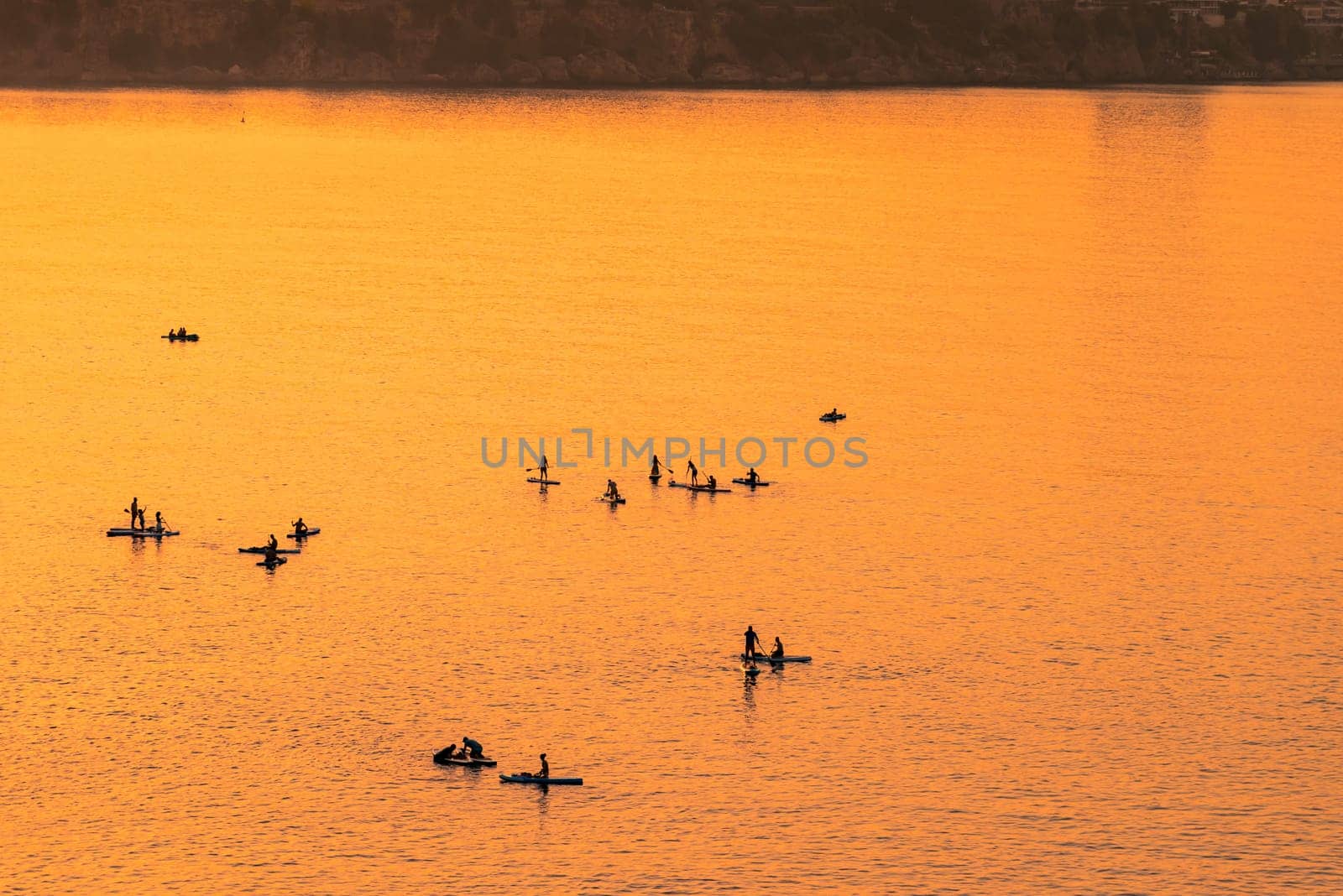 Adventurous people on a stand up paddle board is paddling during a bright and vibrant sunrise by Sonat