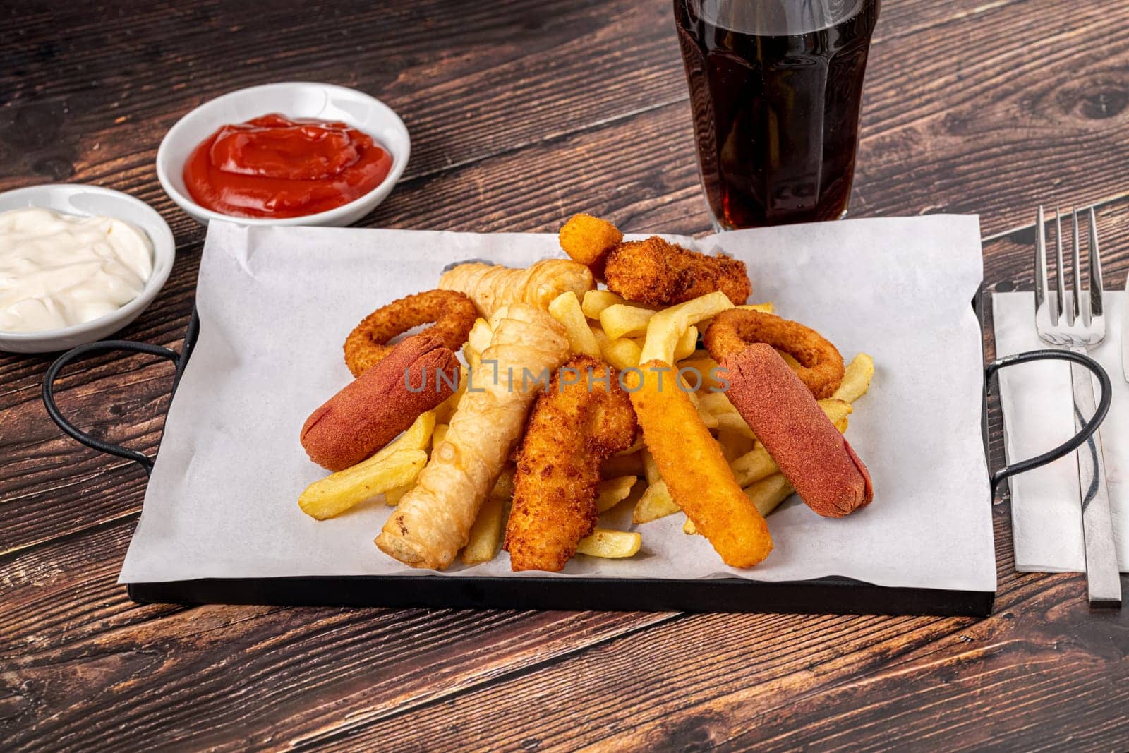 Snack plate with french fries, crispy chicken, cheese sticks, sausage and spring rolls on wooden table