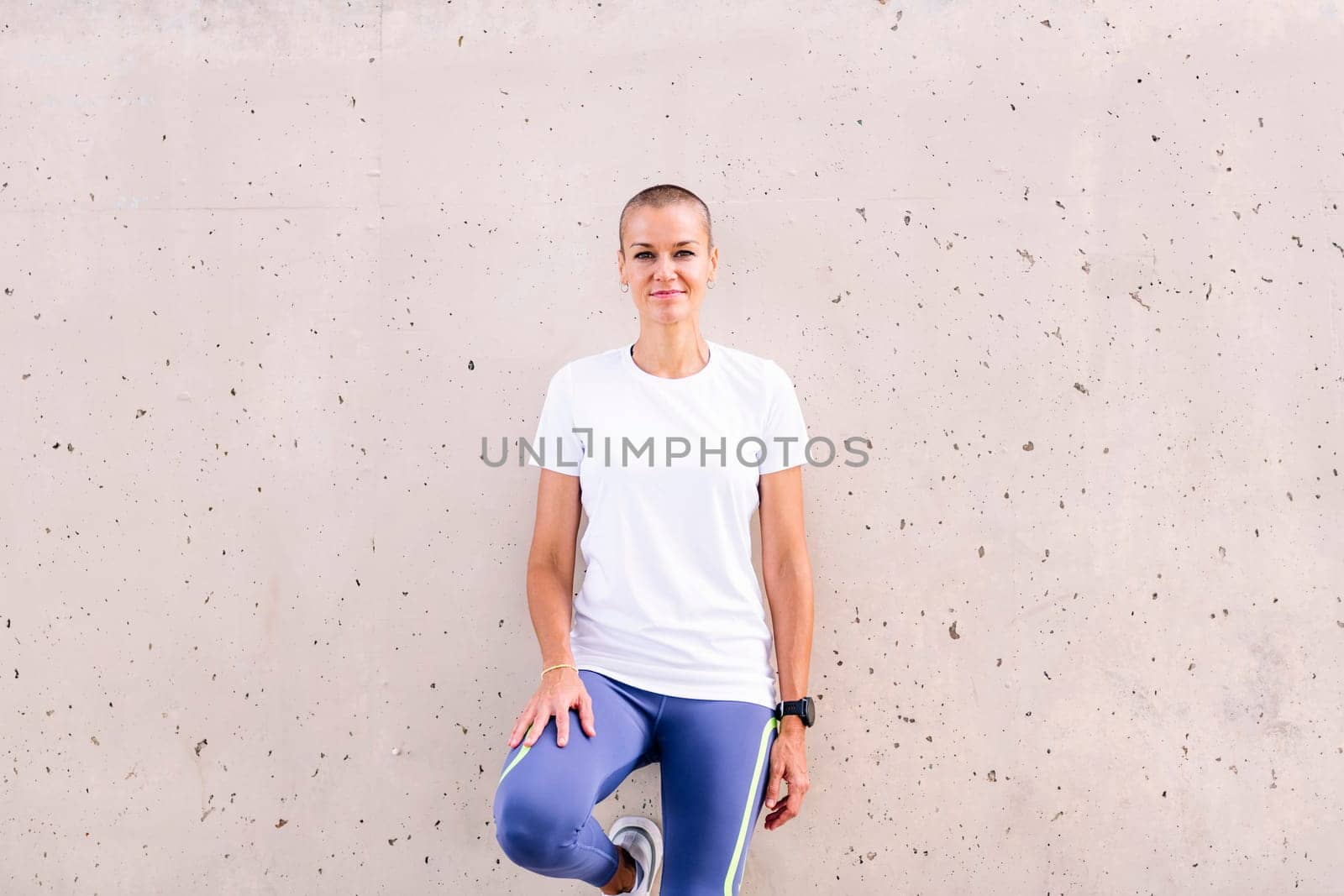 young sports woman smiling happy leaning on a wall looking at camera, concept of active and healthy lifestyle, copy space for text