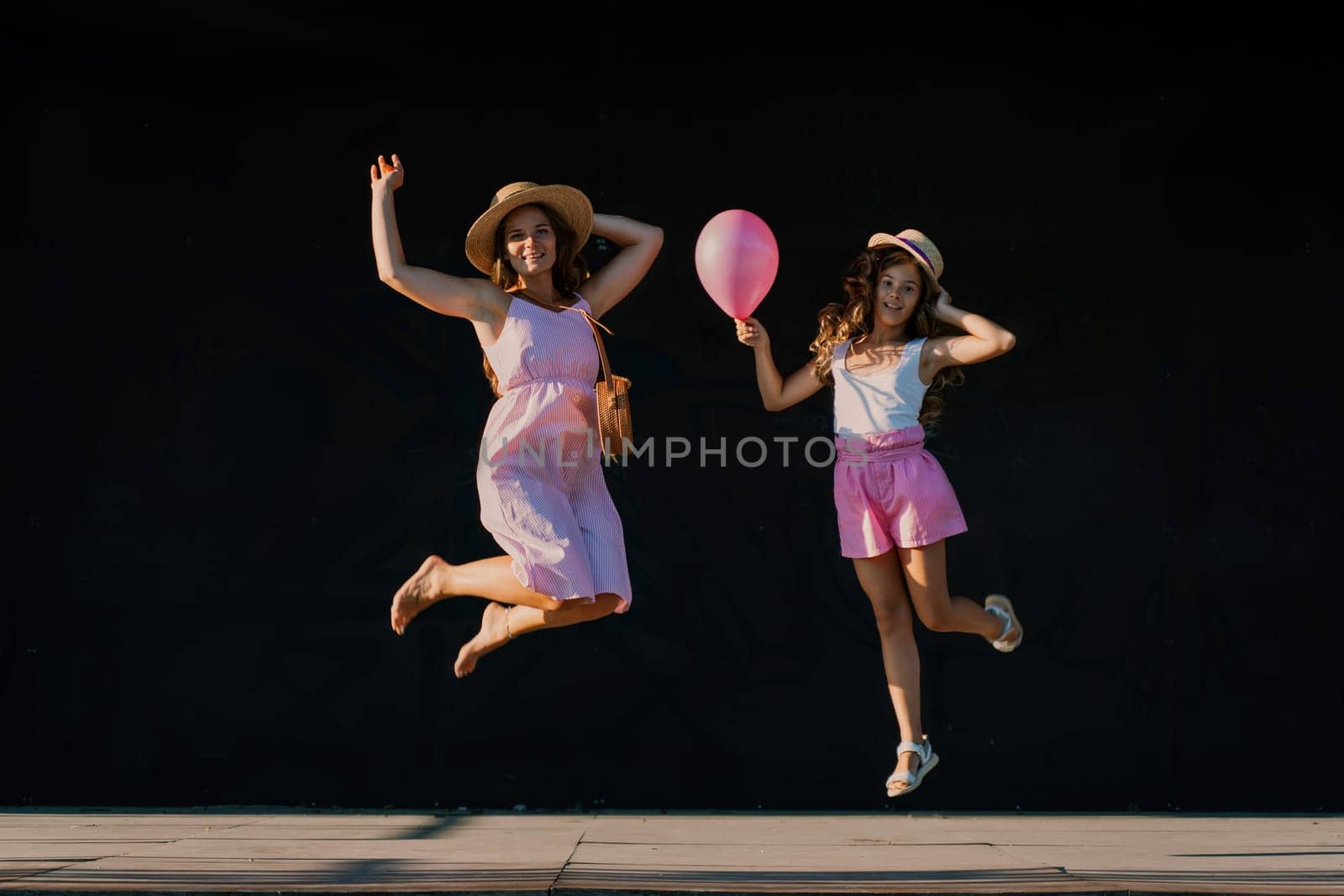 mother and daughter jumping in pink dresses with loose long hair on a black background. Enjoy communicating with each other by Matiunina