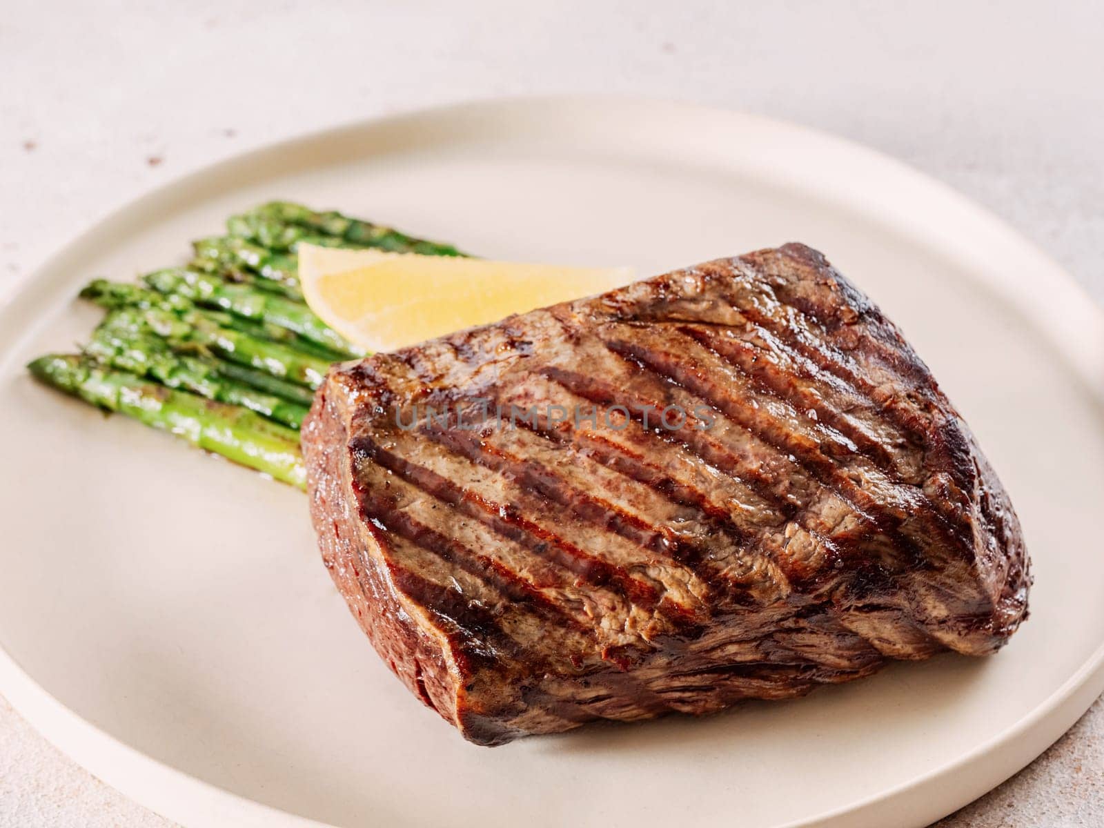 Grilled meat steak on plate with lemon and asparagus on white table background. Food and cuisine concept.