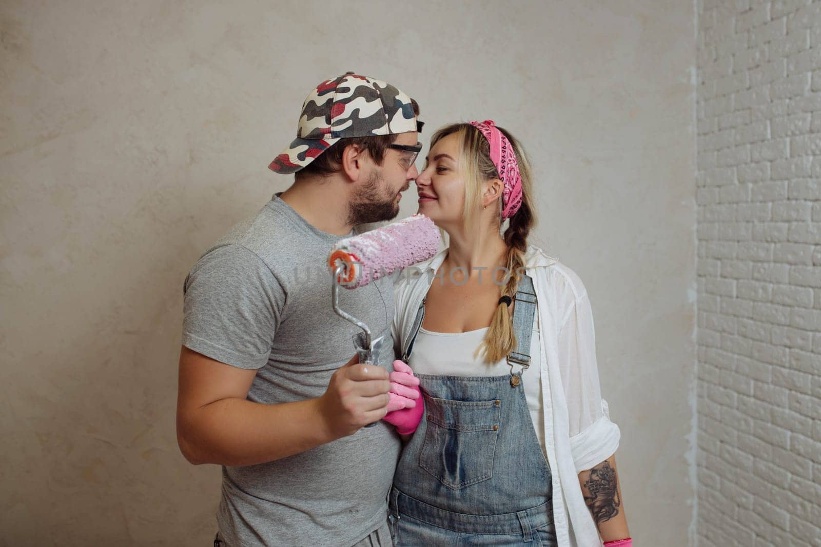 A happy young family makes a dream repair inside the house with their own hands. Husband and wife paint the wall in the room.