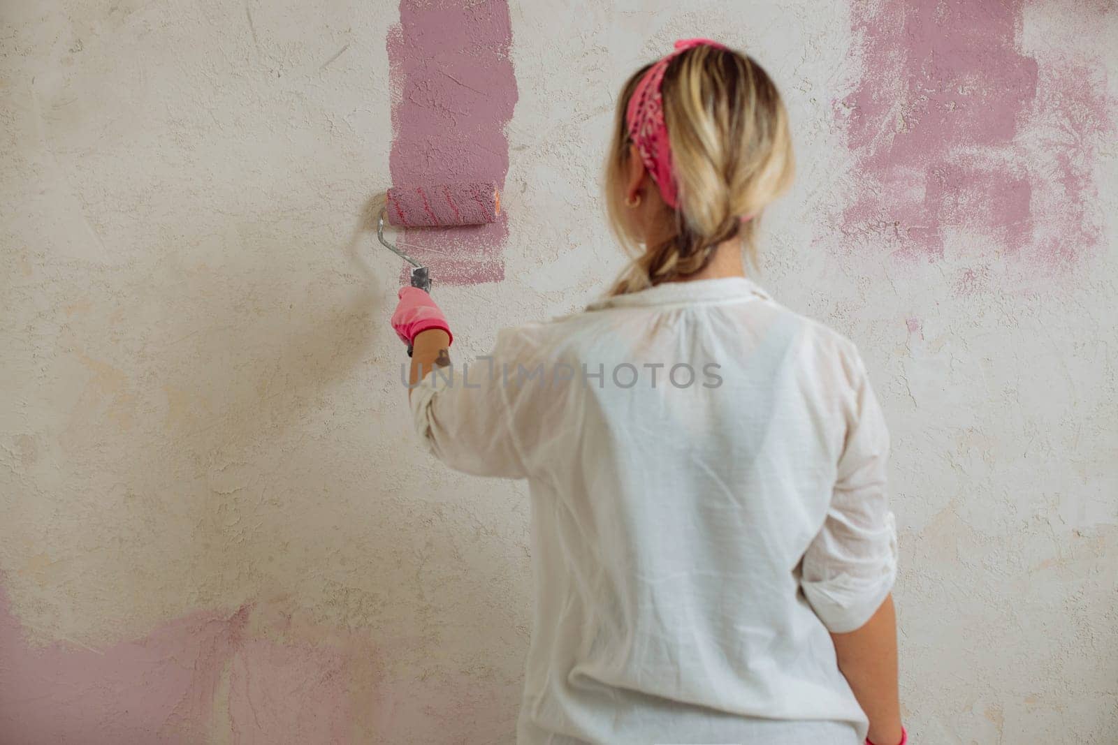 Young woman with the roller painting the wall in new house.