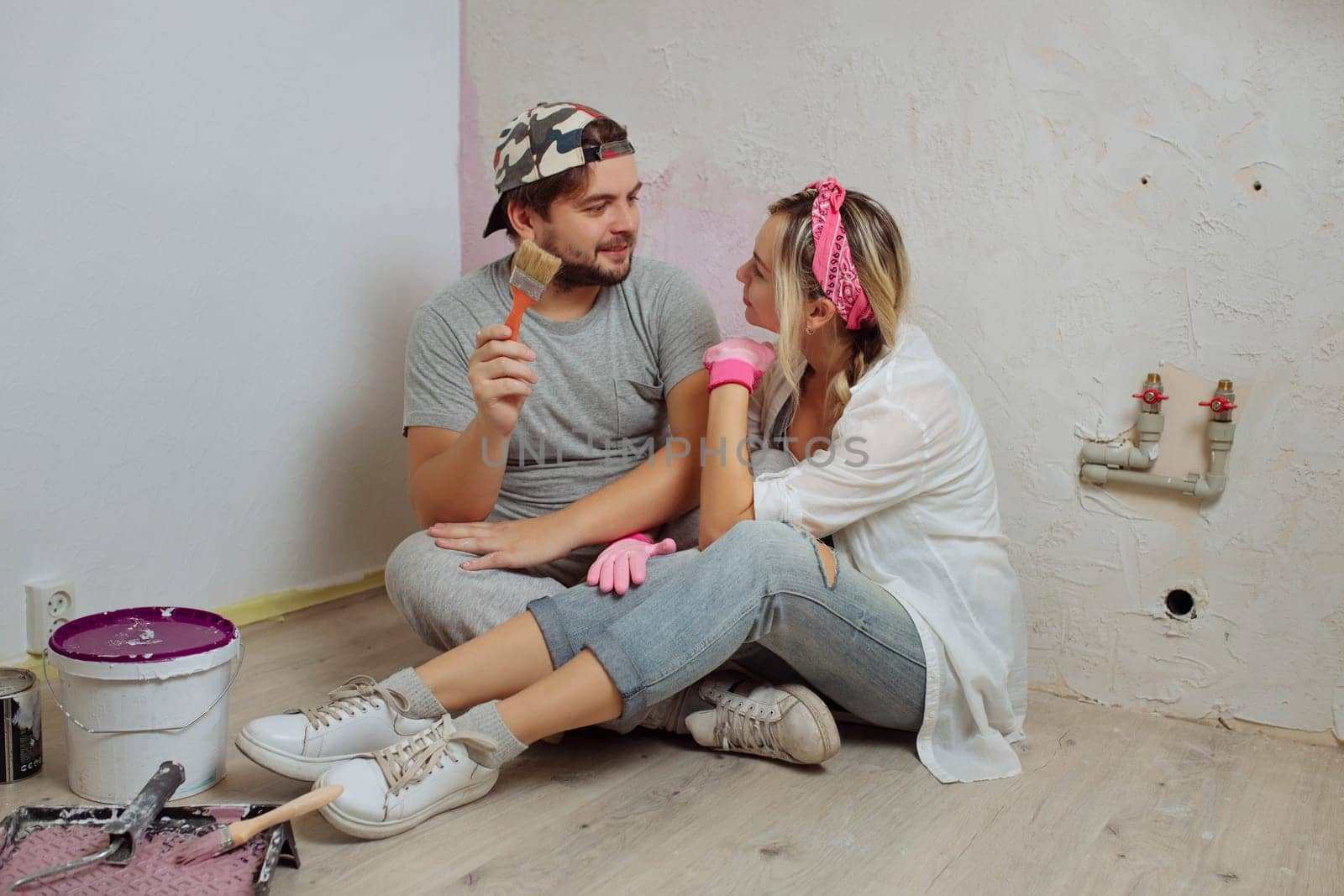 A happy young family makes a dream repair inside the house with their own hands. Husband and wife paint the wall in the room.