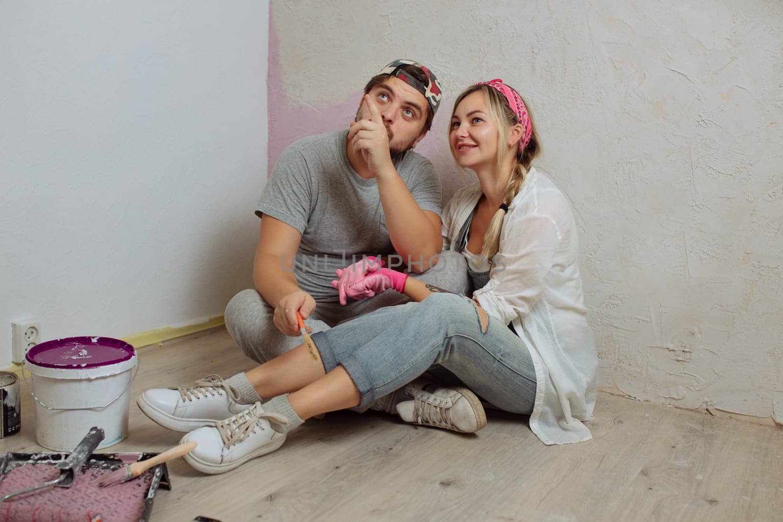 A happy young family makes a dream repair inside the house with their own hands. Husband and wife paint the wall in the room.