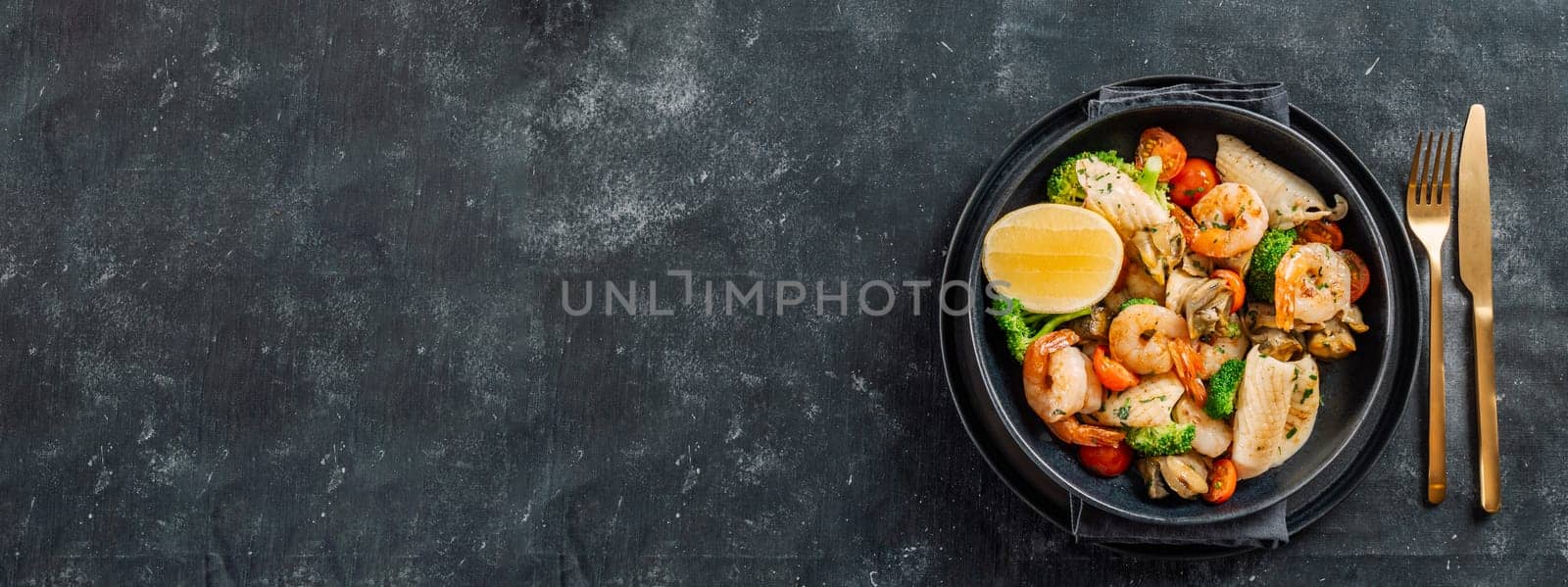 Mixed Seafood Contain Shrimps, Mussels, Calamari Squids and Fish with Broccoli, Cherry Tomato, Lemon on Black dish in restaurant-style platting. Seafood salad on dark background. Top view, copy space, banner