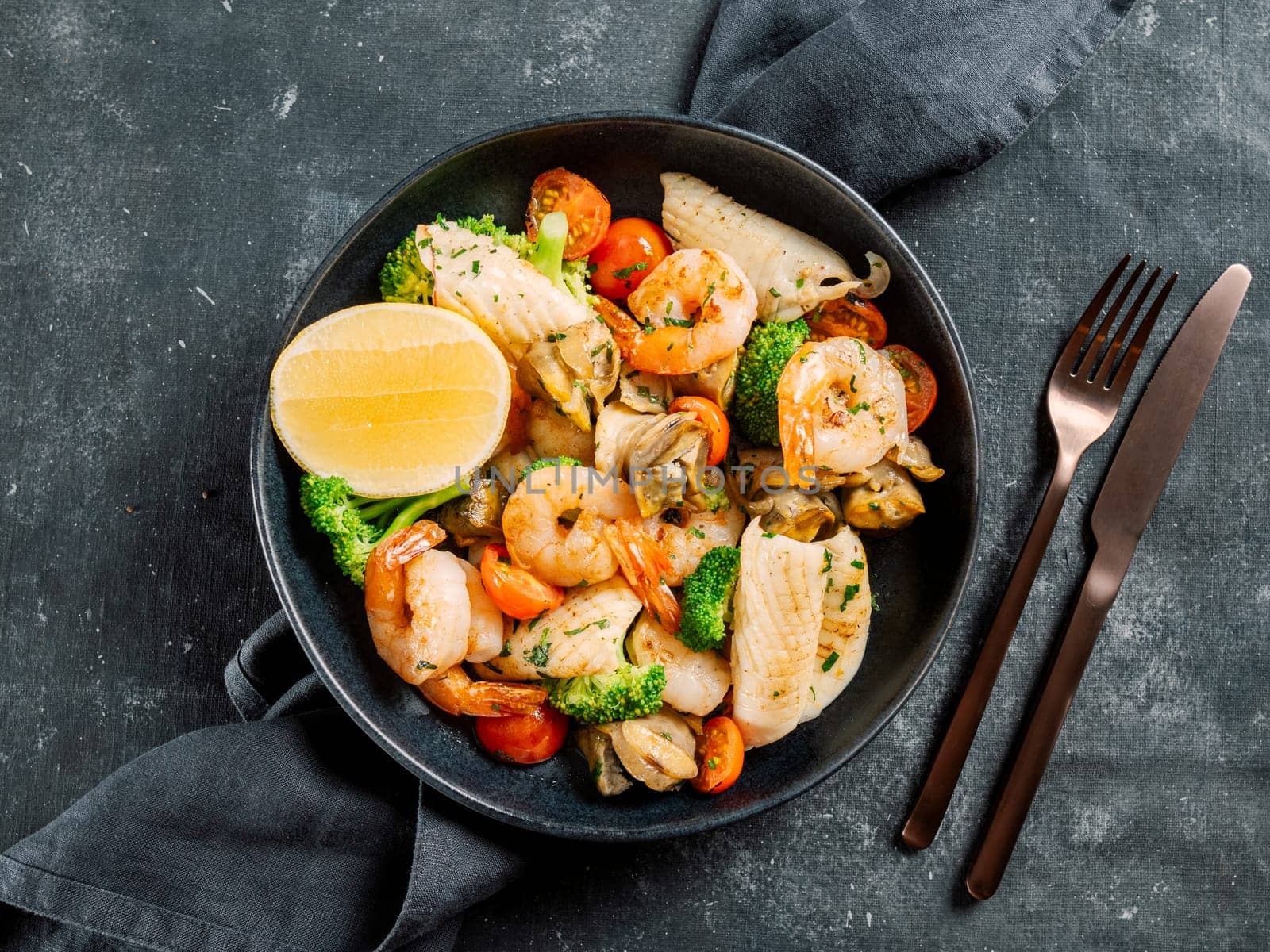 Mixed Seafood Contain Shrimps, Mussels, Calamari Squids and Fish with Broccoli, Cherry Tomato, Lemon on Black dish in restaurant-style platting. Seafood salad on dark background. Top view