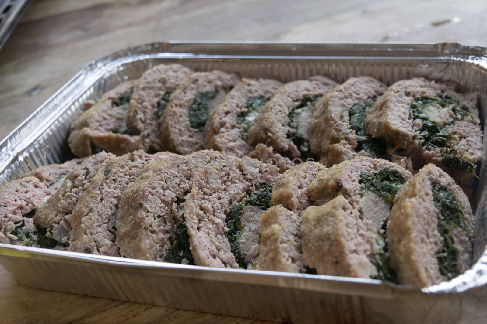 slices of spinach-filled meatloaf lined up in an aluminum container