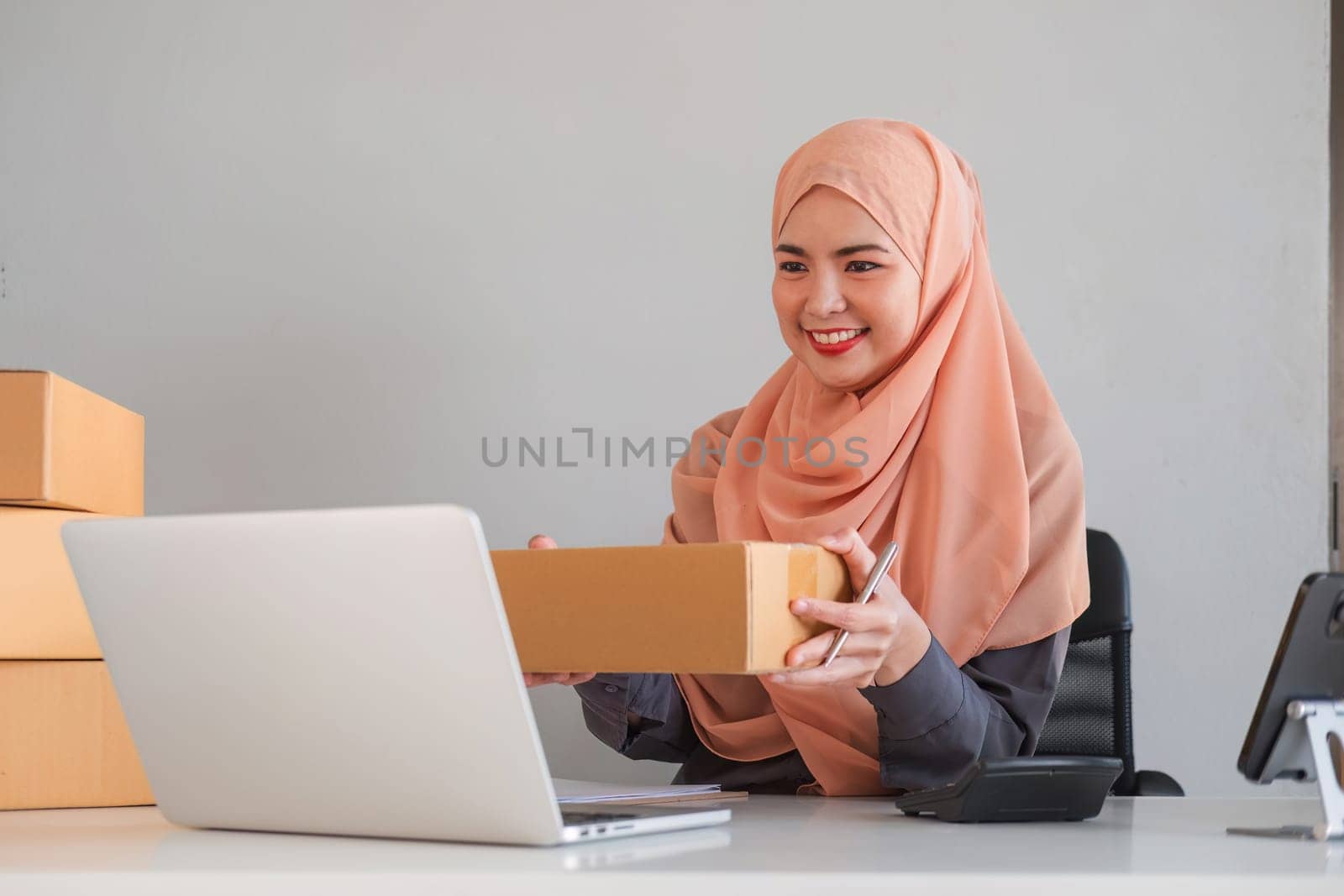Asian Muslim businesswoman checks stock orders and saves them on her home office laptop. small business owner Shipping in online markets The concept of freedom in life by wichayada